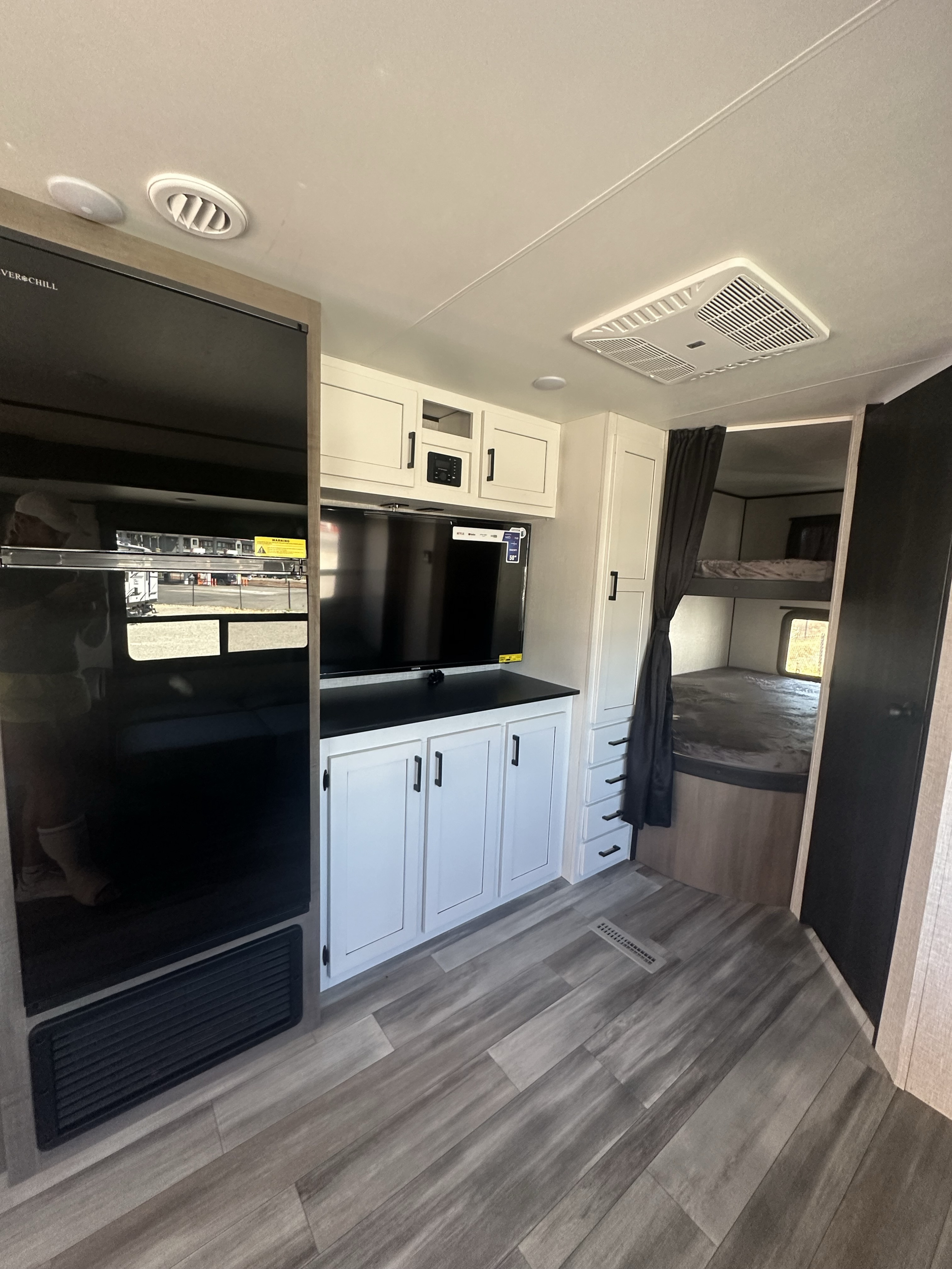 Modern RV rental interior showing a large fridge, media center with TV, and bunk beds on the right, plus wood-look flooring.. Starcraft Autumn Ridge 2024