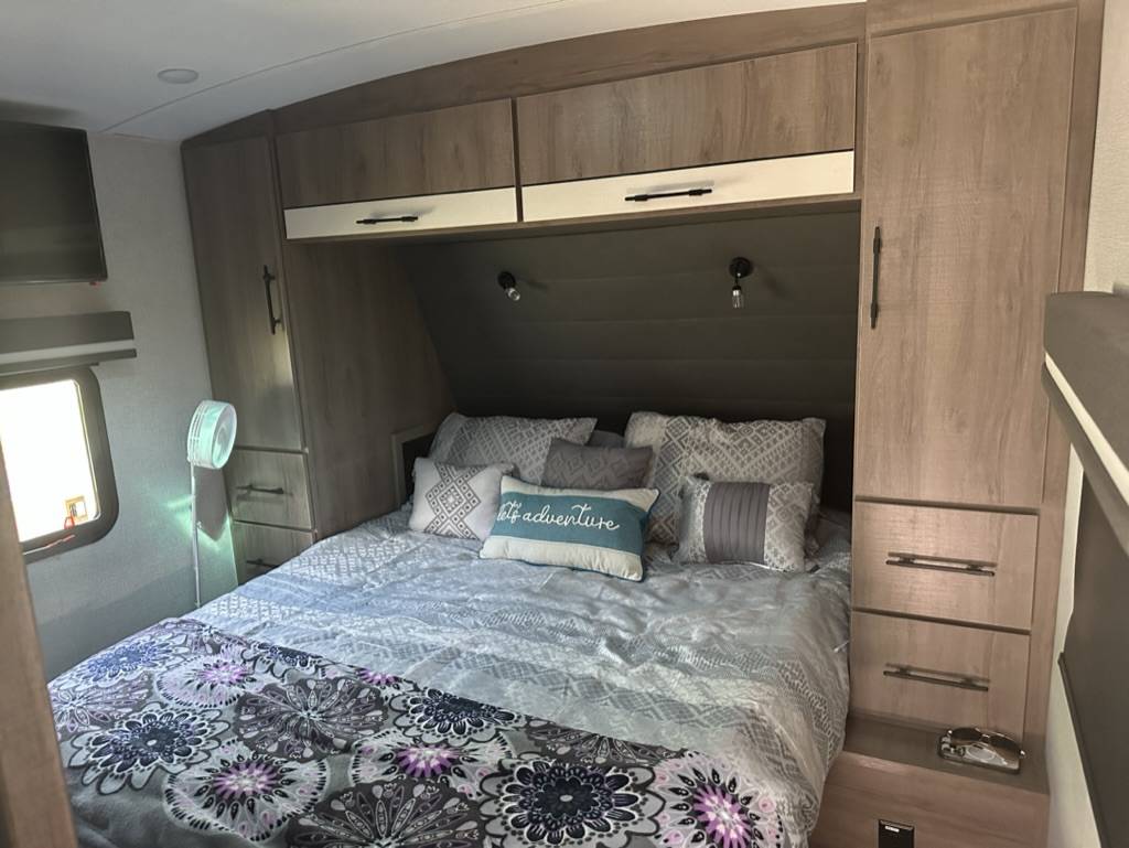 Inside an RV rental, this bedroom offers a queen bed, overhead cabinets, and built-in storage, ideal for travel.. Grand Design Imagine 2023