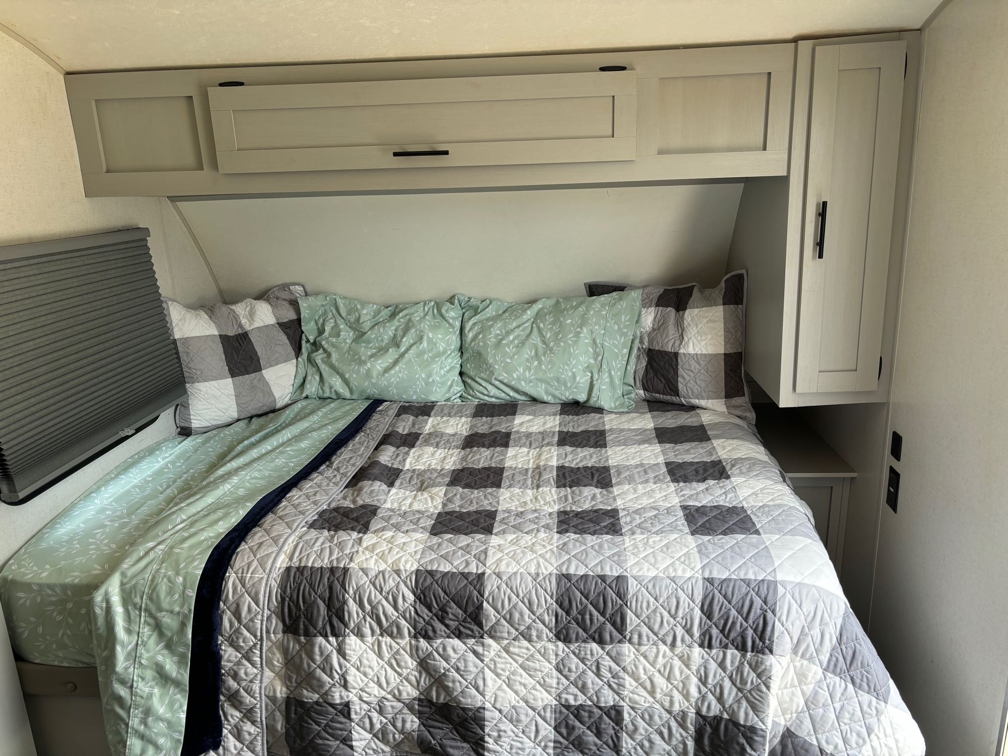 Inside a comfy RV rental bedroom: bed with plaid quilt, green sheets, overhead cabinets, and window blind.. Forest River Salem FSX PLATINUM 2021