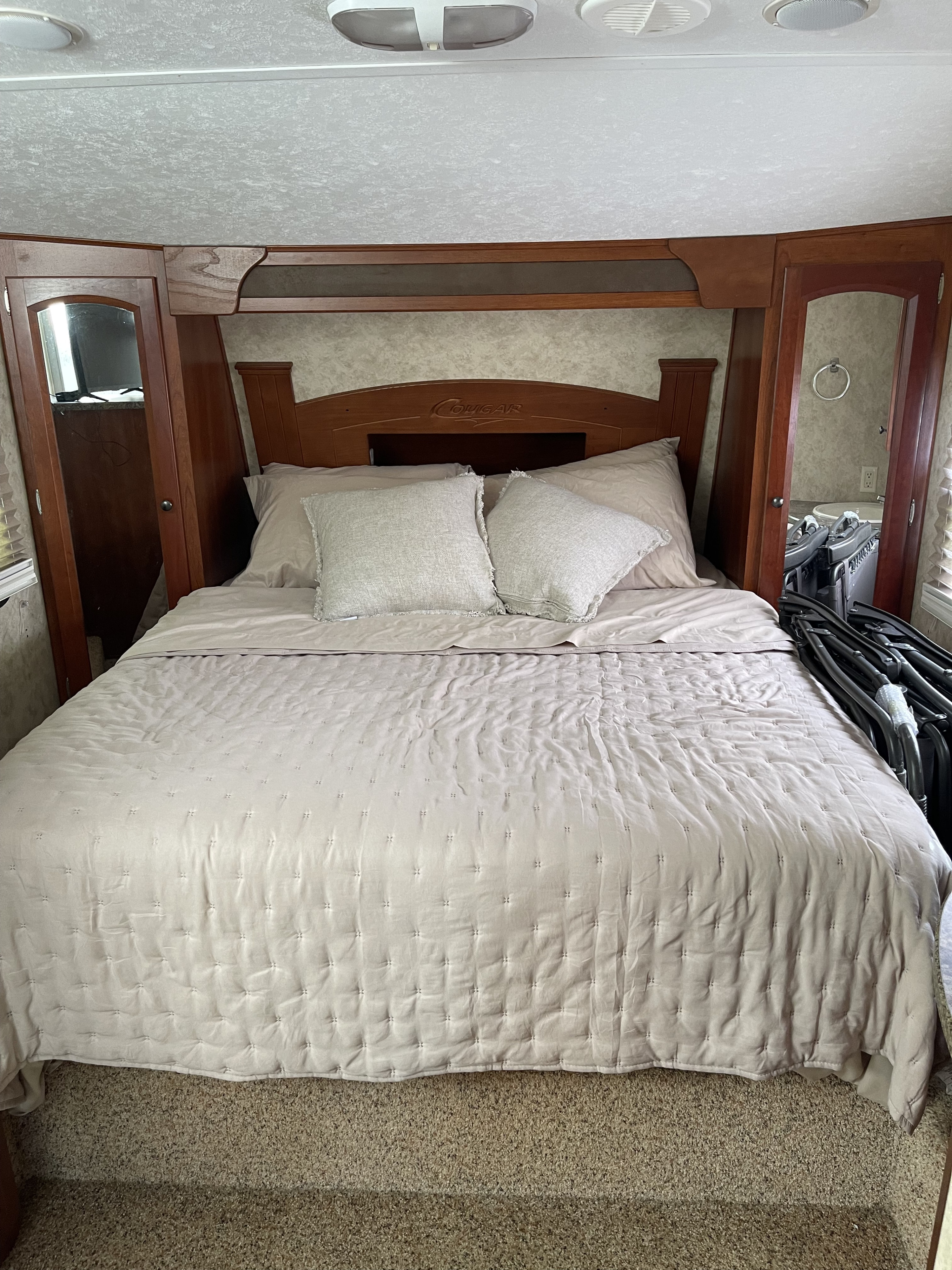 Cozy RV rental bedroom: large bed with light bedding, wooden headboard, built-in storage. Ideal for comfortable travel.. Keystone RV Cougar 2010