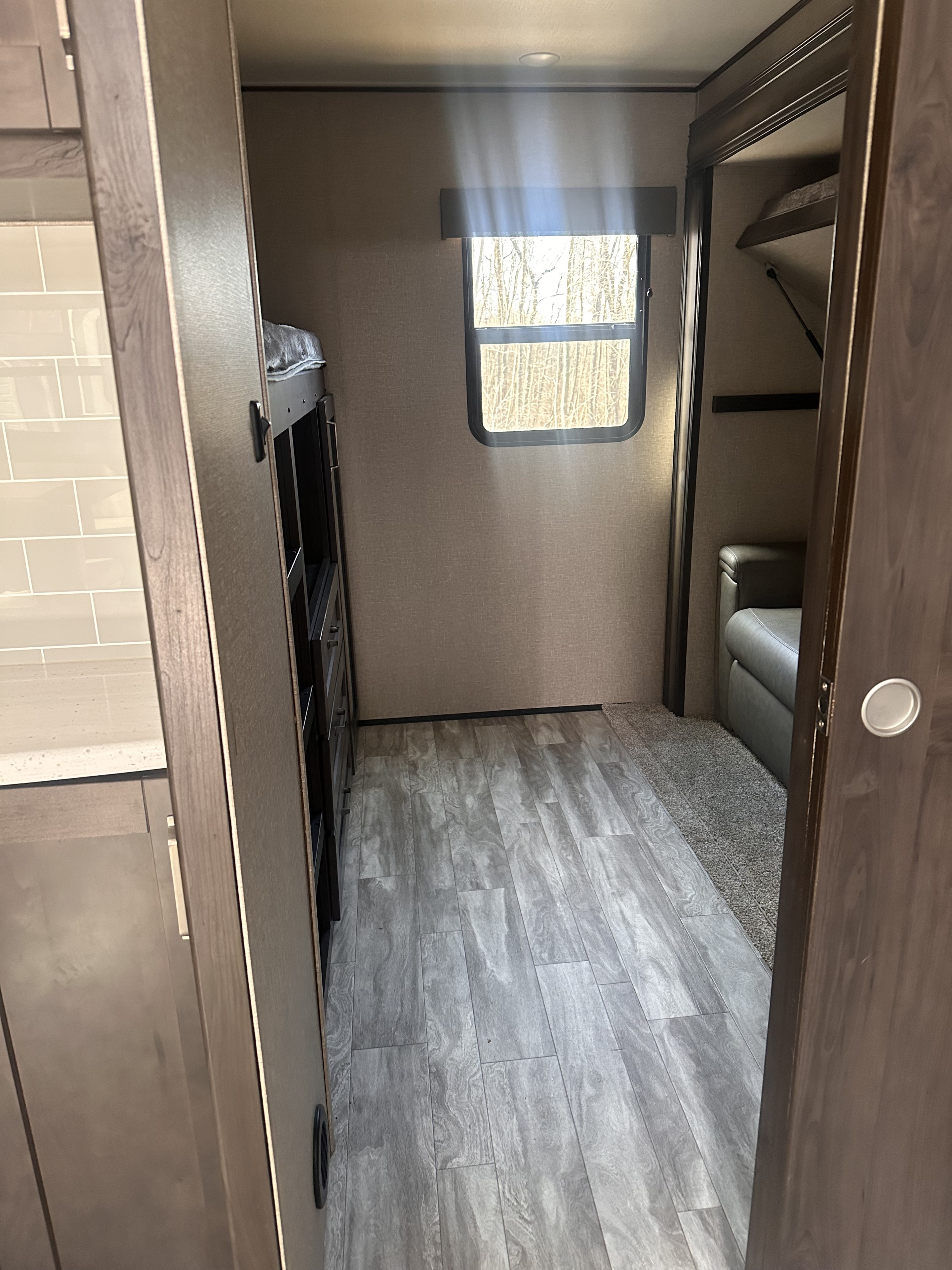 View of an rv rental's bunk room, featuring wood-look flooring, a window overlooking trees, and a sofa visible through an open door.. Grand Design Reflection 2022