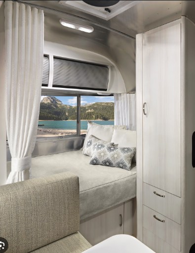 Cozy RV rental interior with a bed by a scenic lake view, light wood cabinets, and modern amenities for comfortable travel.. Airstream Bambi 2021