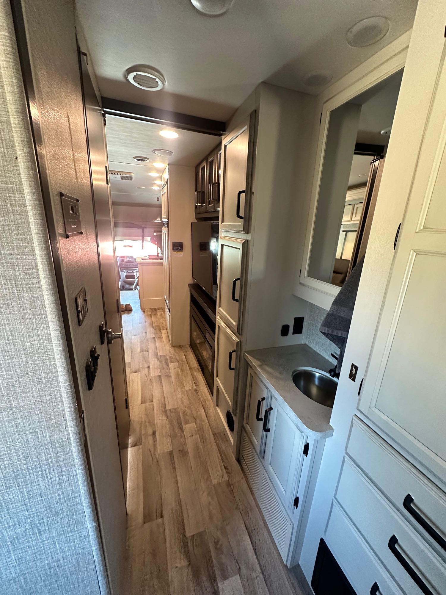 Step inside this RV rental, showcasing a functional hallway with a compact vanity, ample storage, and warm lighting leading to the cockpit.. Jayco Greyhawk 2023