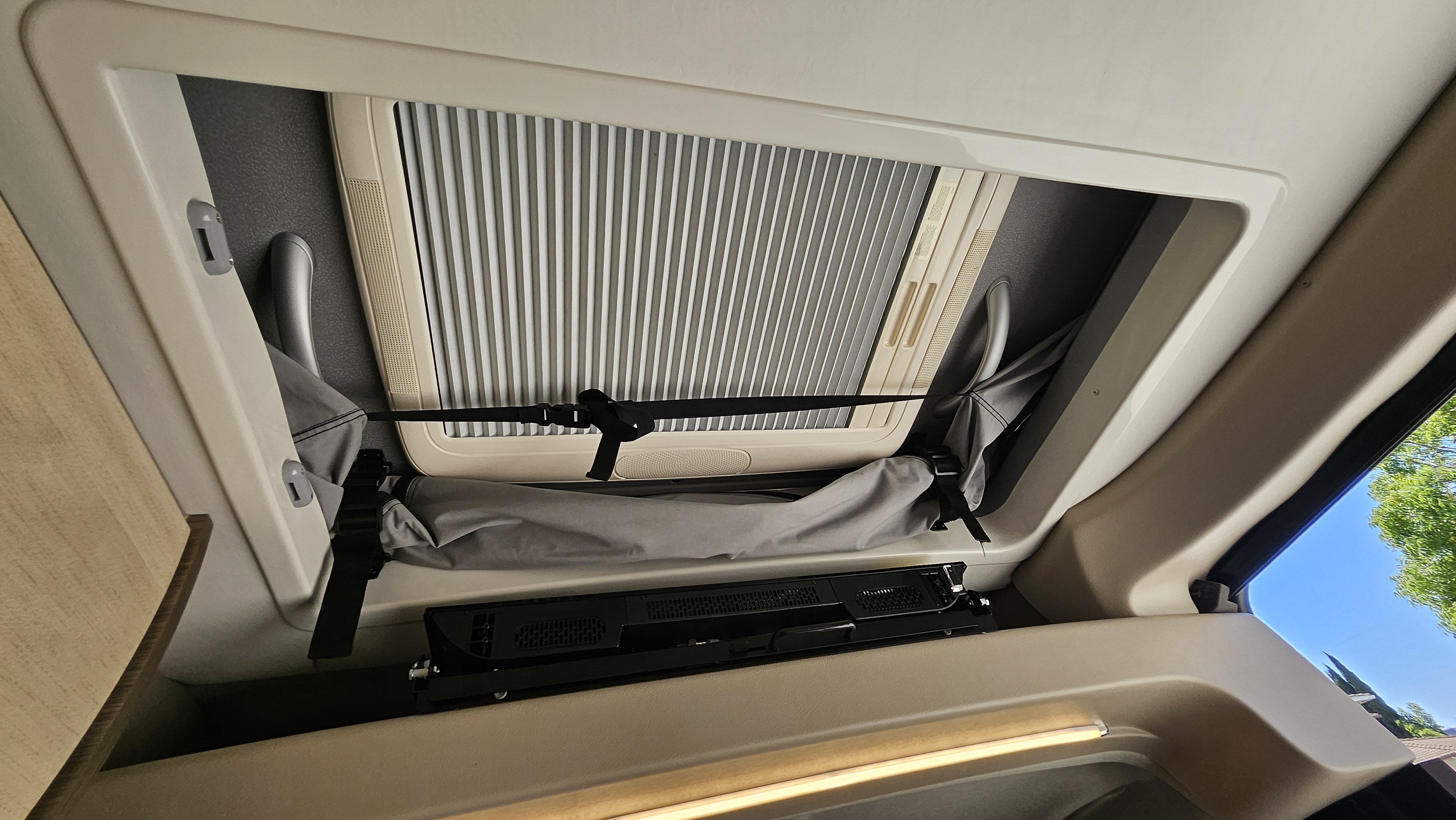 rv rental interior: overhead view of a skylight with closed blind, strapped storage, and mounted entertainment unit.. Entegra Coach Ethos 2024
