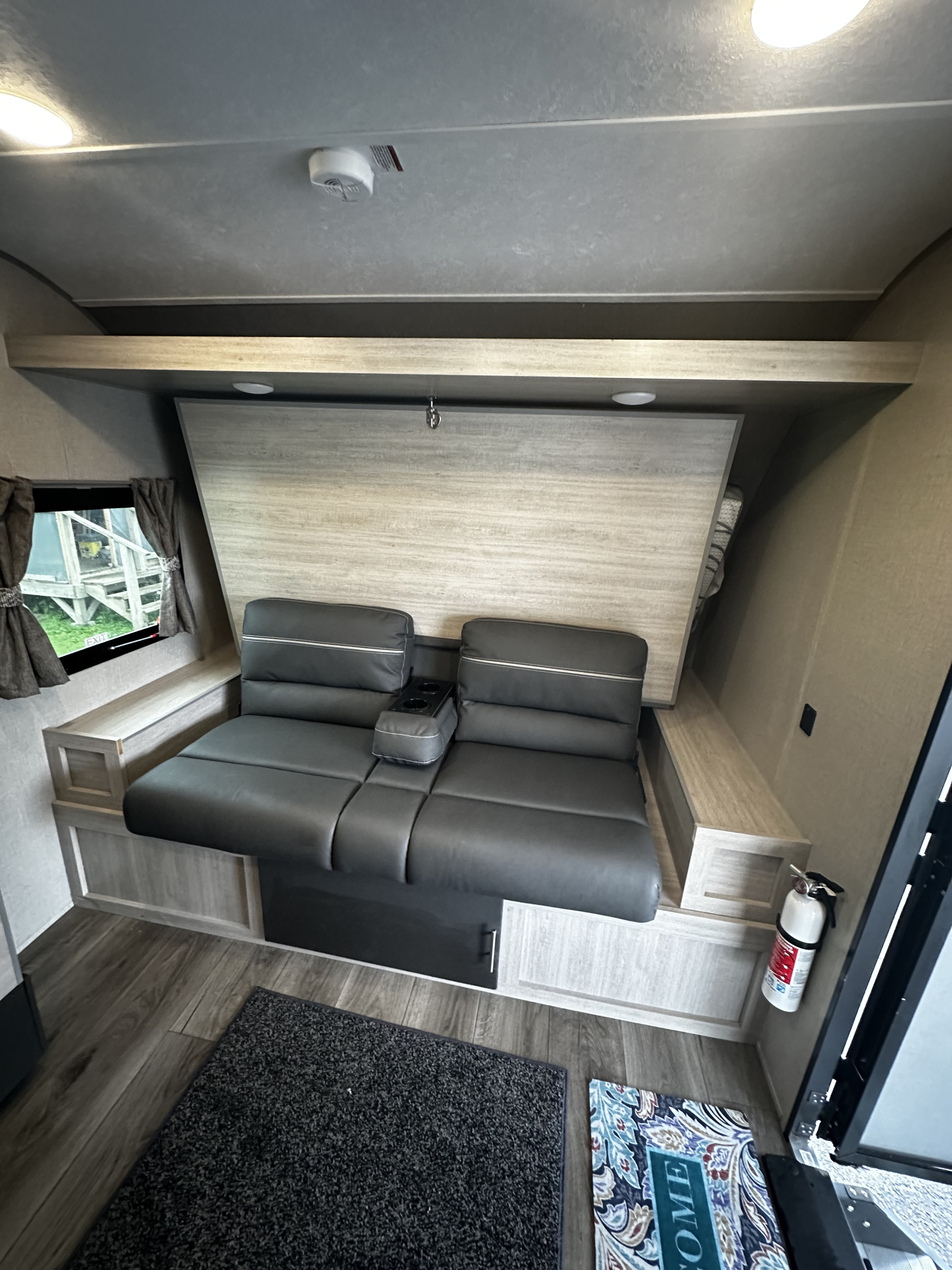 RV rental interior with a dark gray sofa (cup holders visible) that converts to a bed, set against light wood paneling, for comfort on the road.. Coachmen Catalina 2022