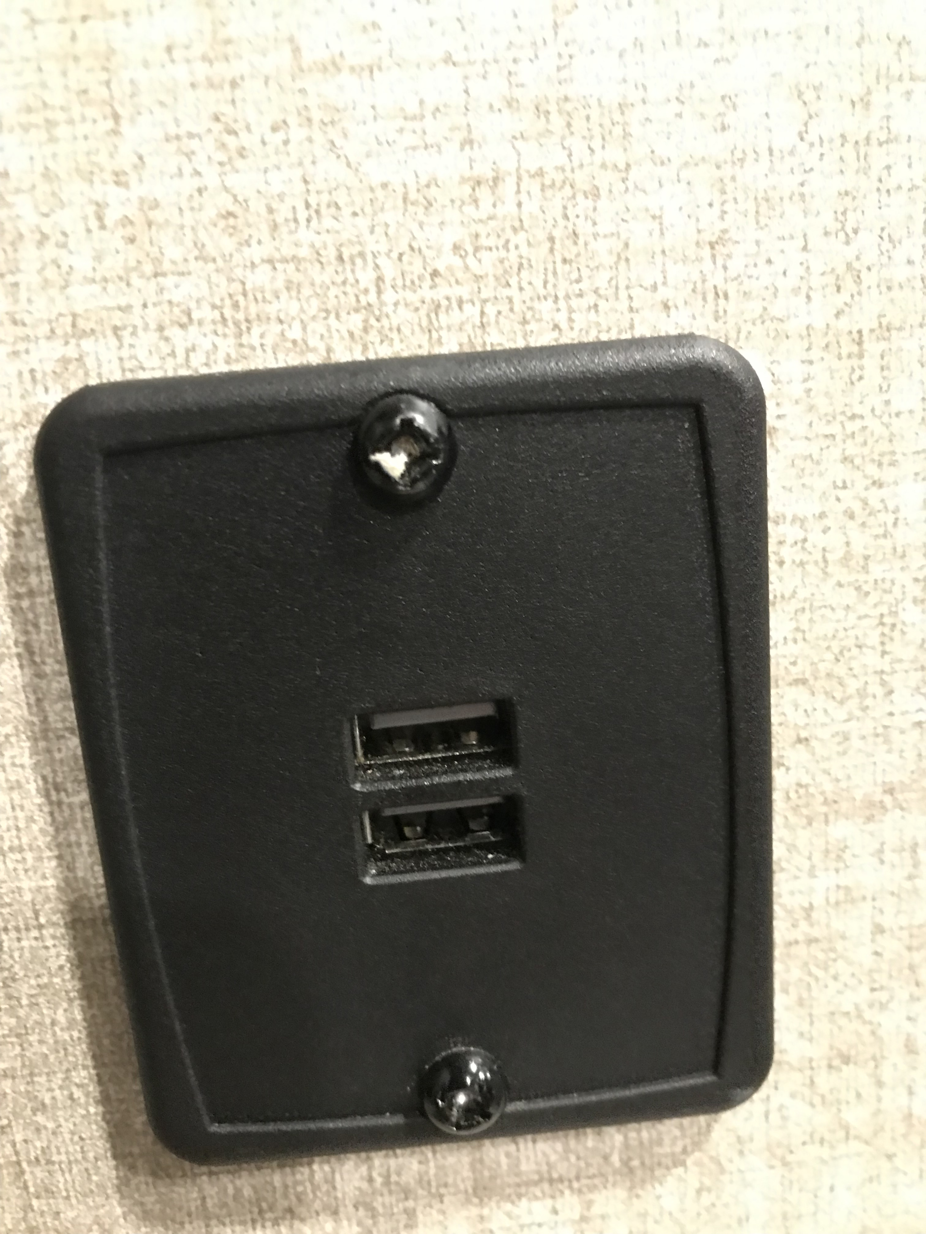 Close-up of an RV rental's black, wall-mounted dual USB charging port with two visible screws, offering convenient power on trips.. Coachmen Catalina 2022