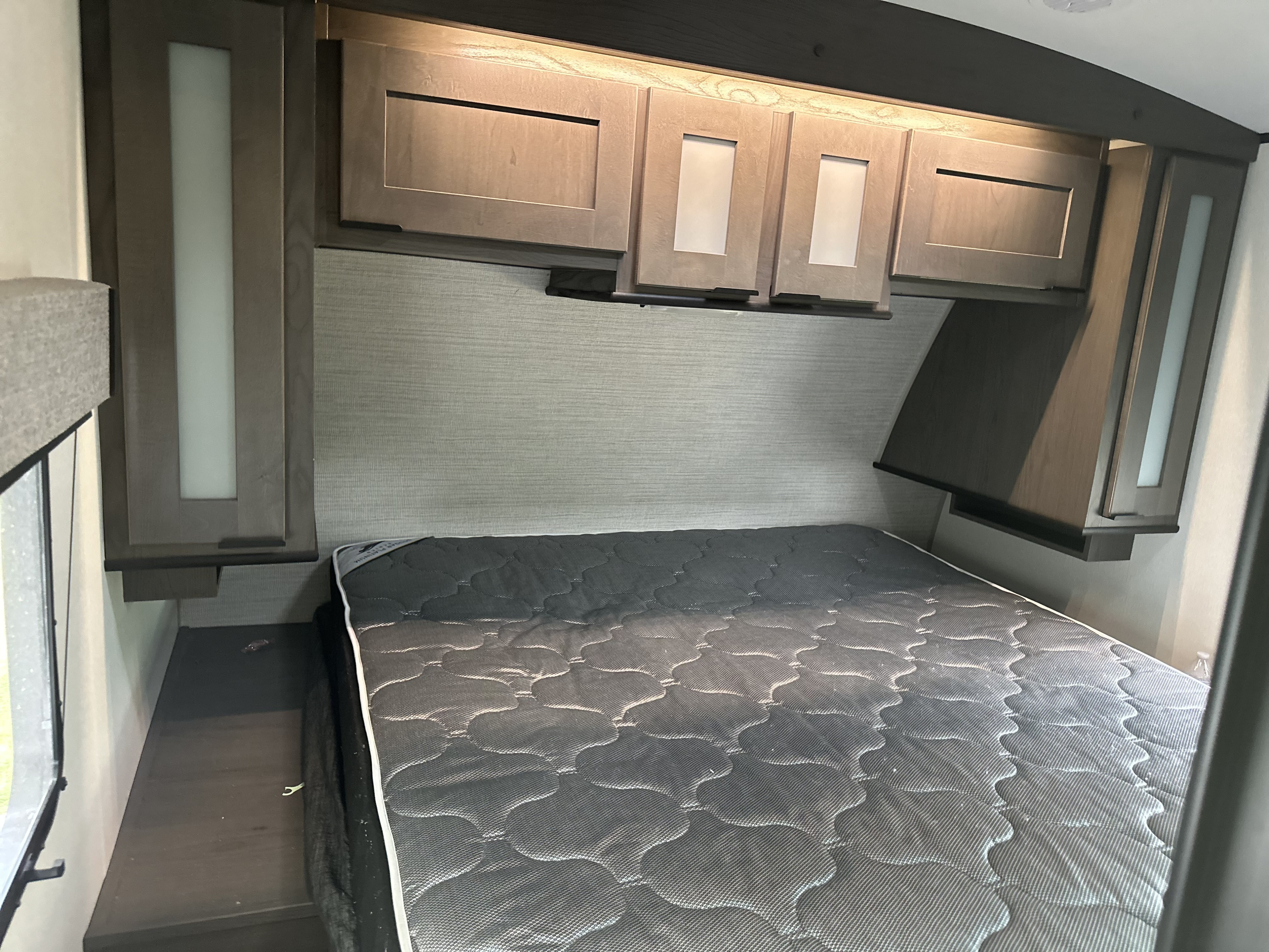Cozy RV rental bedroom featuring a grey mattress, light wood overhead cabinets, and built-in storage for a comfortable stay.. Mpg 2500BH MPG 2021