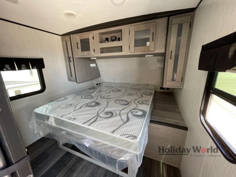 RV rental bedroom featuring a new, plastic-covered bed, overhead cabinets, and a side window. Perfect for your travels.. Heartland RVs Mallard 2021
