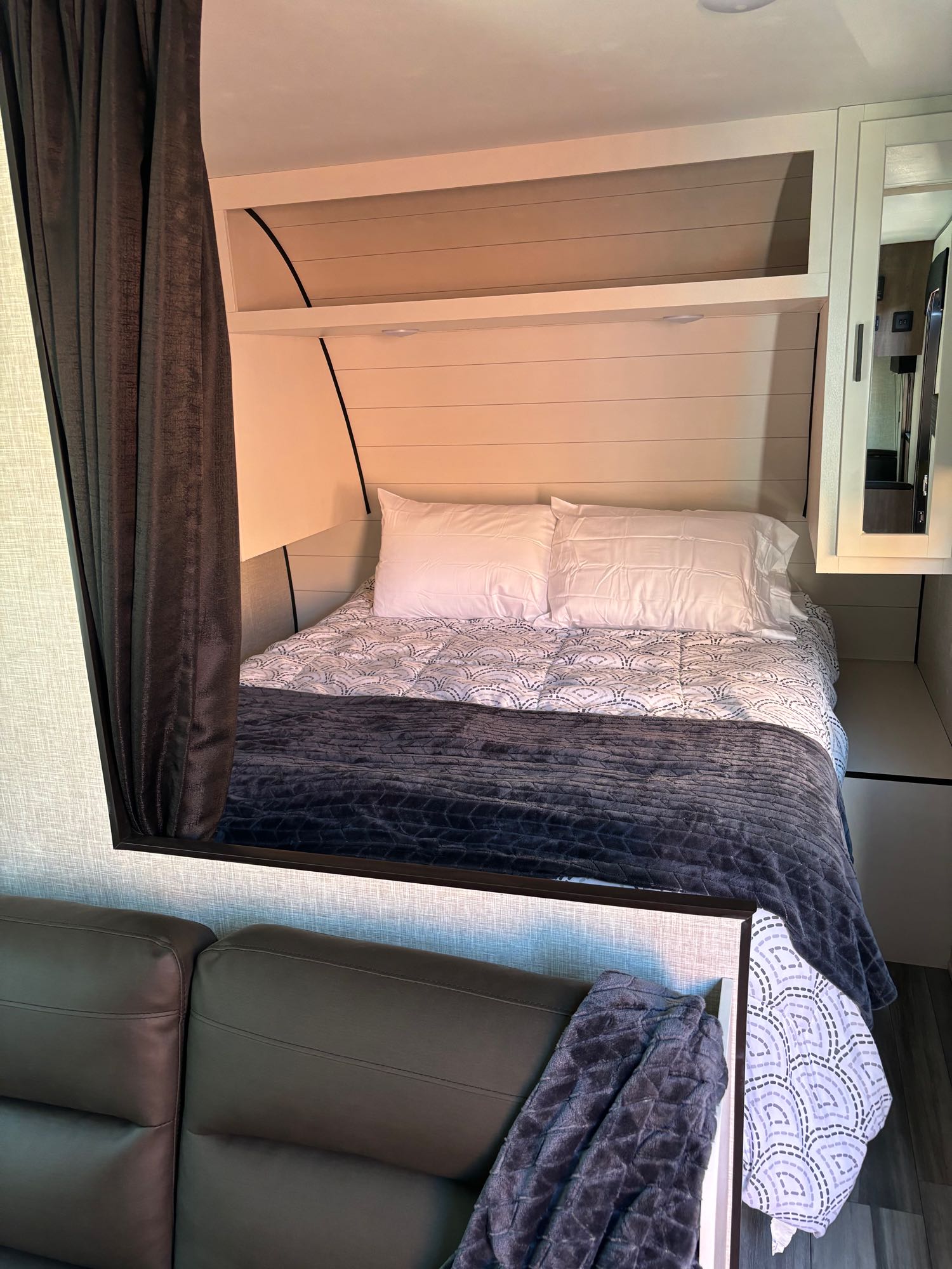 Cozy RV rental bed area with white shiplap walls, dark blanket, and adjacent seating. Ideal for relaxing.. Jayco Jay Flight SLX 2024