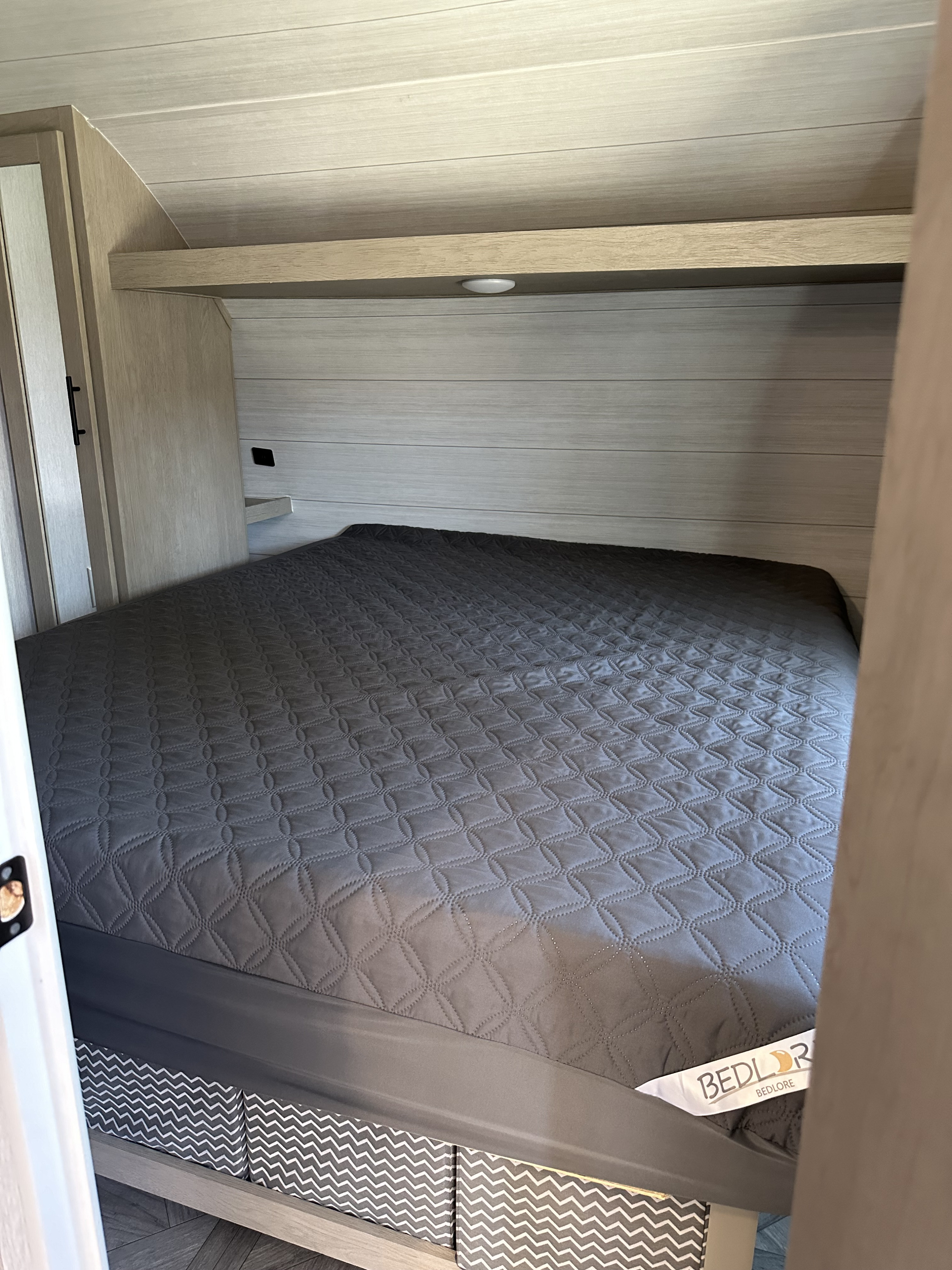 Interior of an RV rental bedroom with a neatly made bed, quilted comforter, and light wood paneled walls. Built-in storage visible.. Forest River Salem Cruise Lite 2023