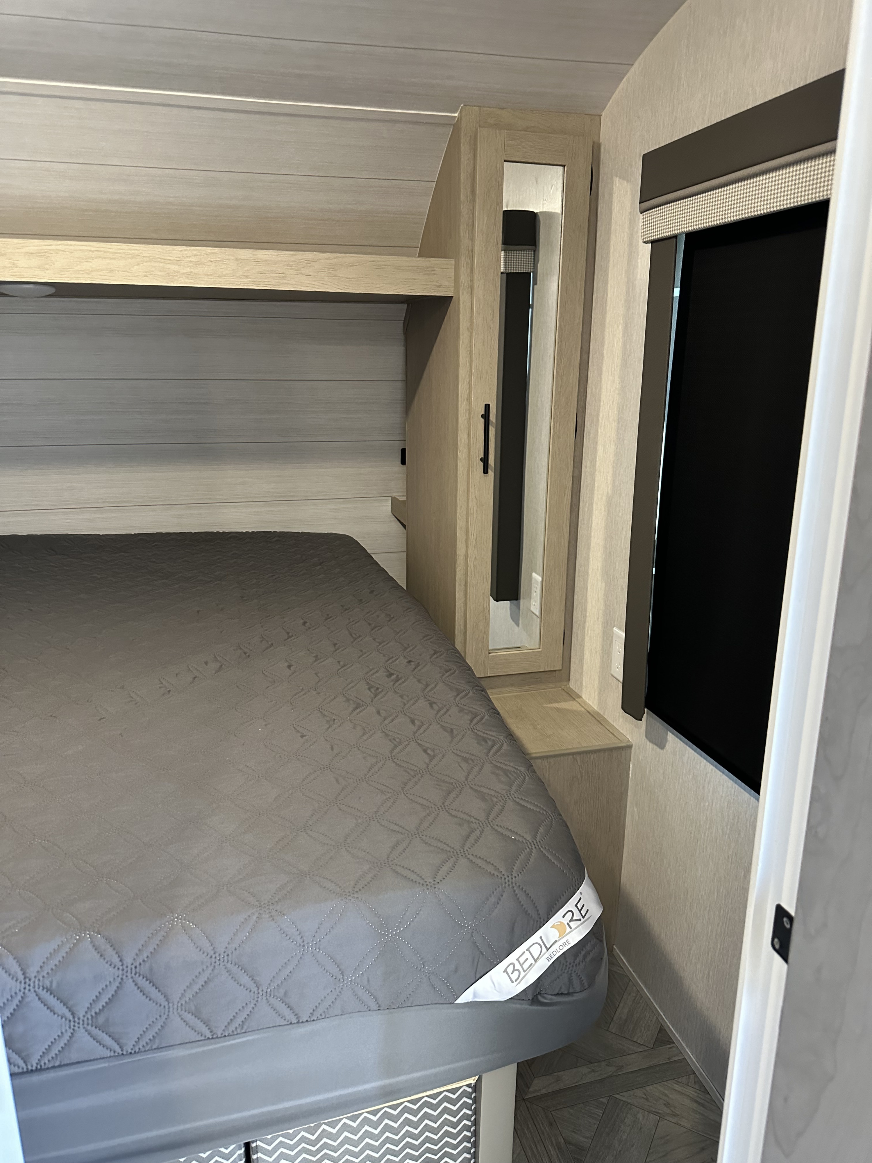 RV rental bedroom interior featuring a comfortable gray bed, overhead storage, mirrored wardrobe, and modern window treatment.. Forest River Salem Cruise Lite 2023