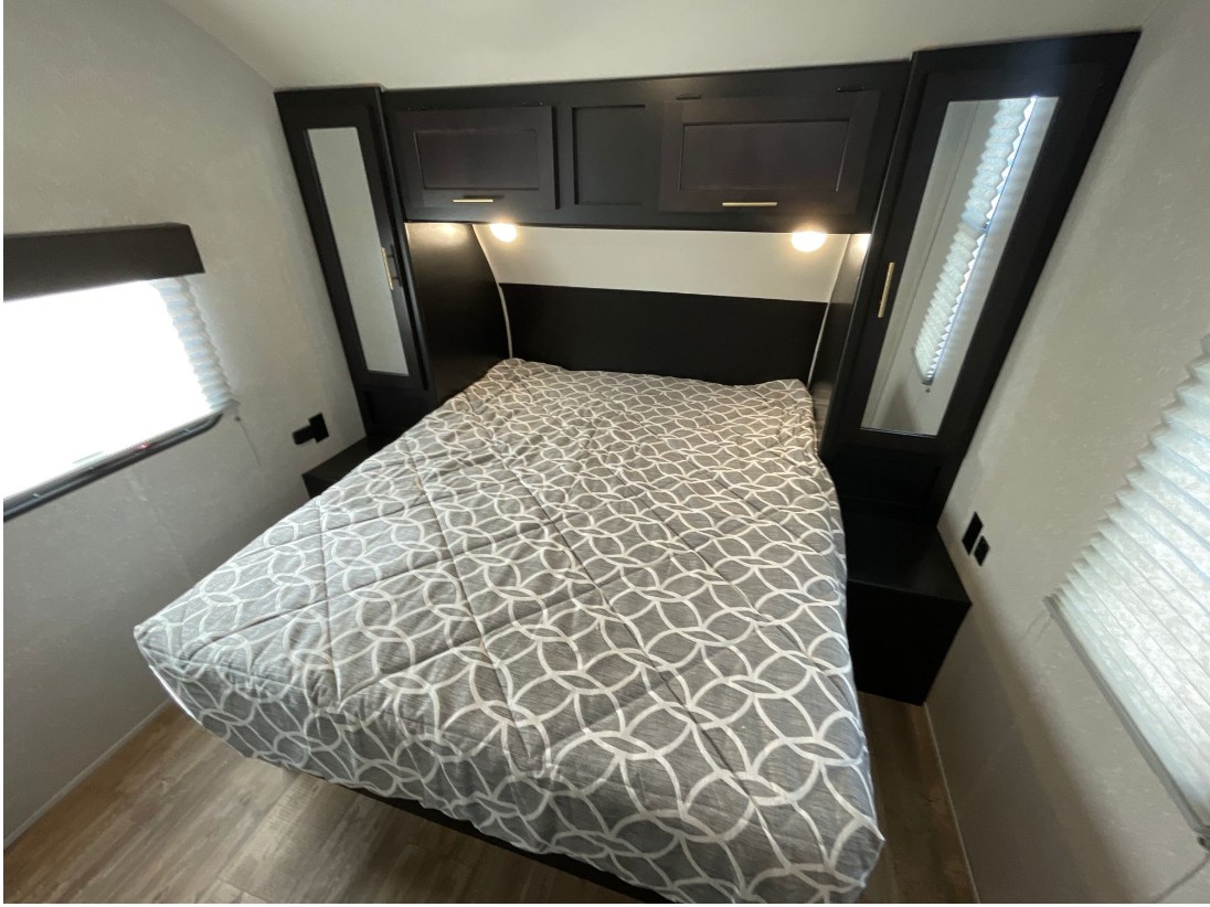 Spacious RV rental bedroom features a comfy bed, overhead cabinets, and mirrored wardrobes.. Forest River Cherokee Grey Wolf Black Label 2021