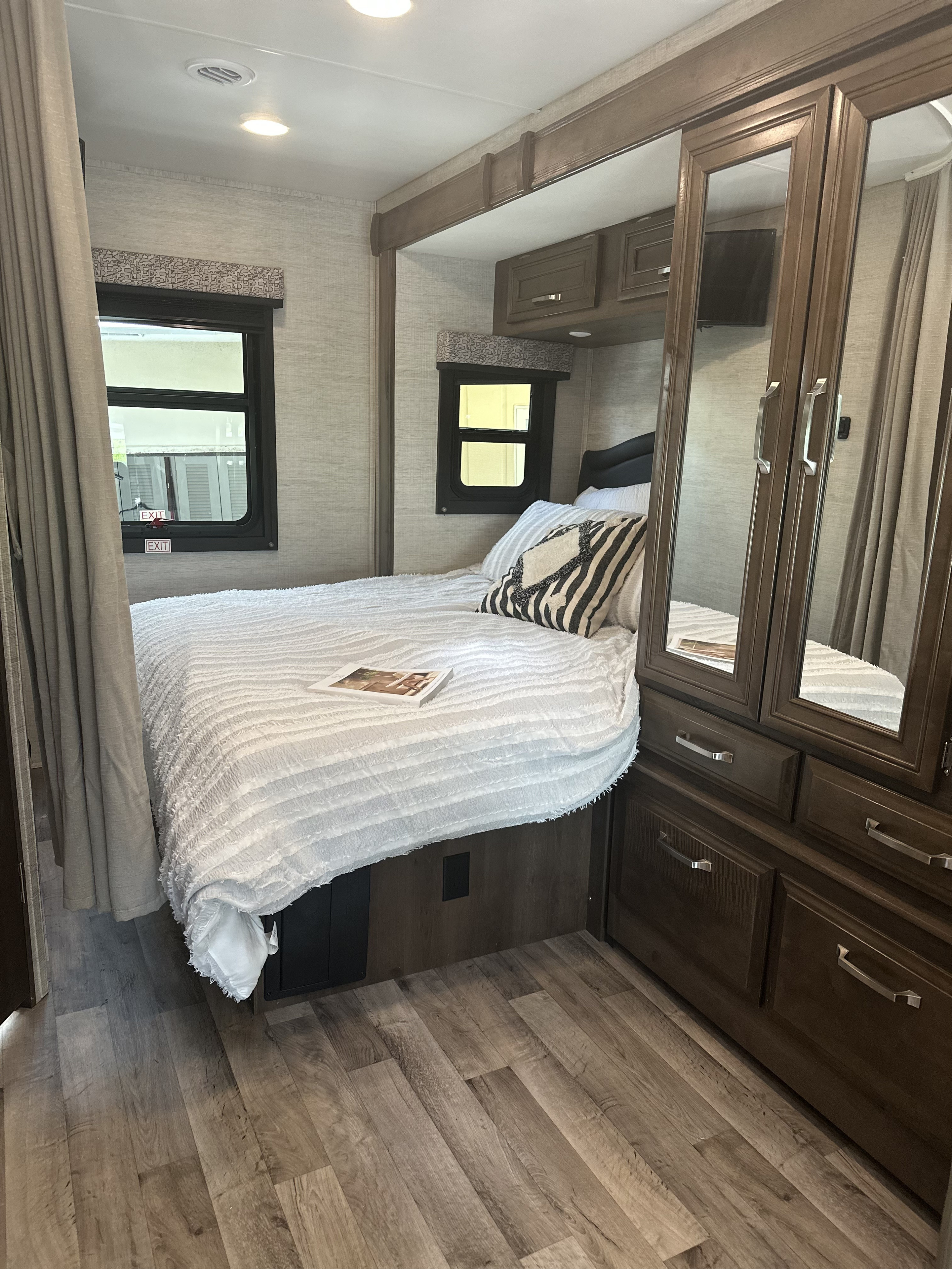 Cozy RV rental bedroom showing a bed, mirrored cabinet, windows, and wood-look floor, offering comfort on the road.. Jayco Melbourne 2022