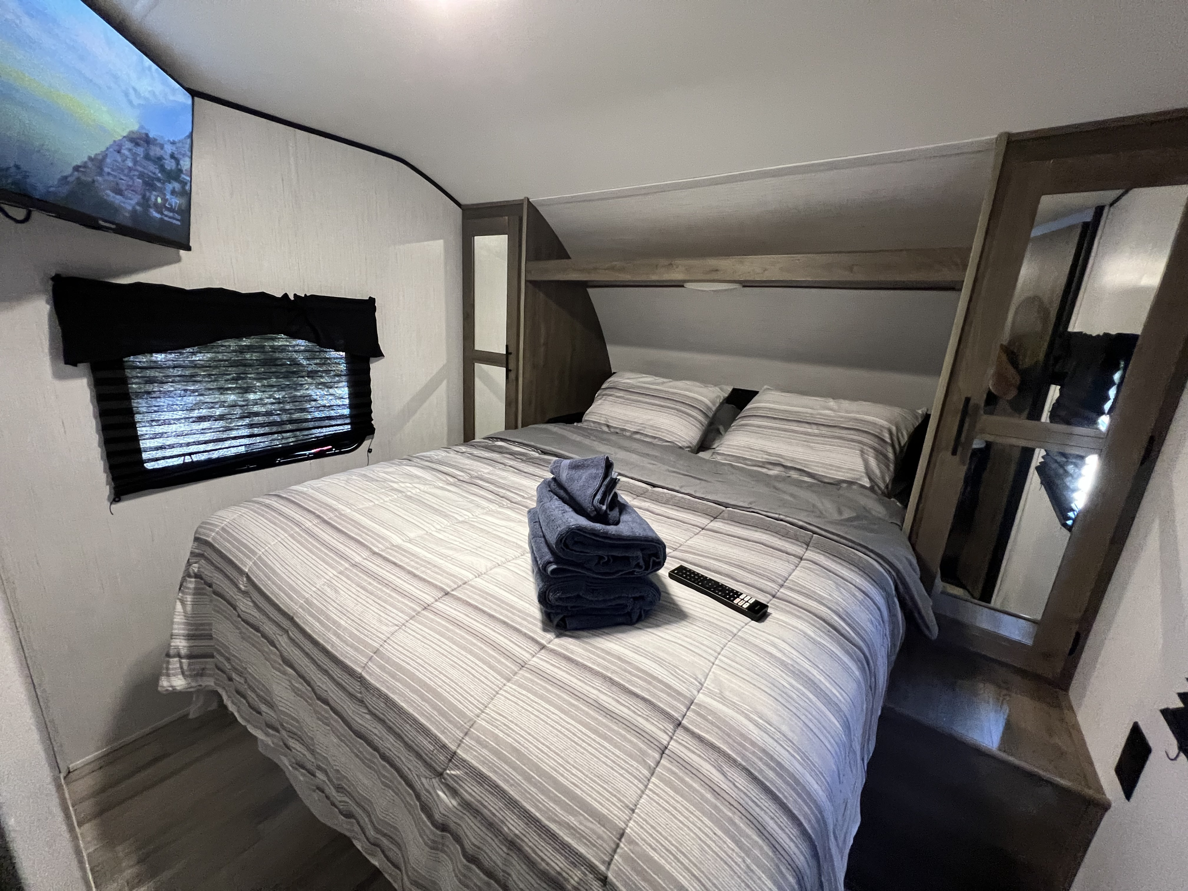 Cozy RV rental bedroom featuring a comfortable bed with striped linens, blue towels, TV, and mirrored storage.. Heartland RVs Pioneer 2022