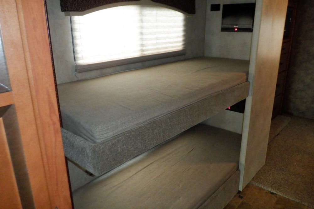 RV rental interior showing two comfy bunk beds with light mattresses, a window with blinds, and a wall-mounted TV.. Thor Hurricane 2012