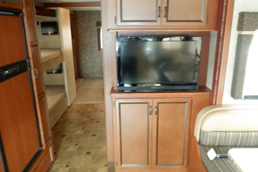 View inside an RV rental: bunk beds with personal TVs, entertainment center, dinette, and refrigerator.. Thor Hurricane 2012