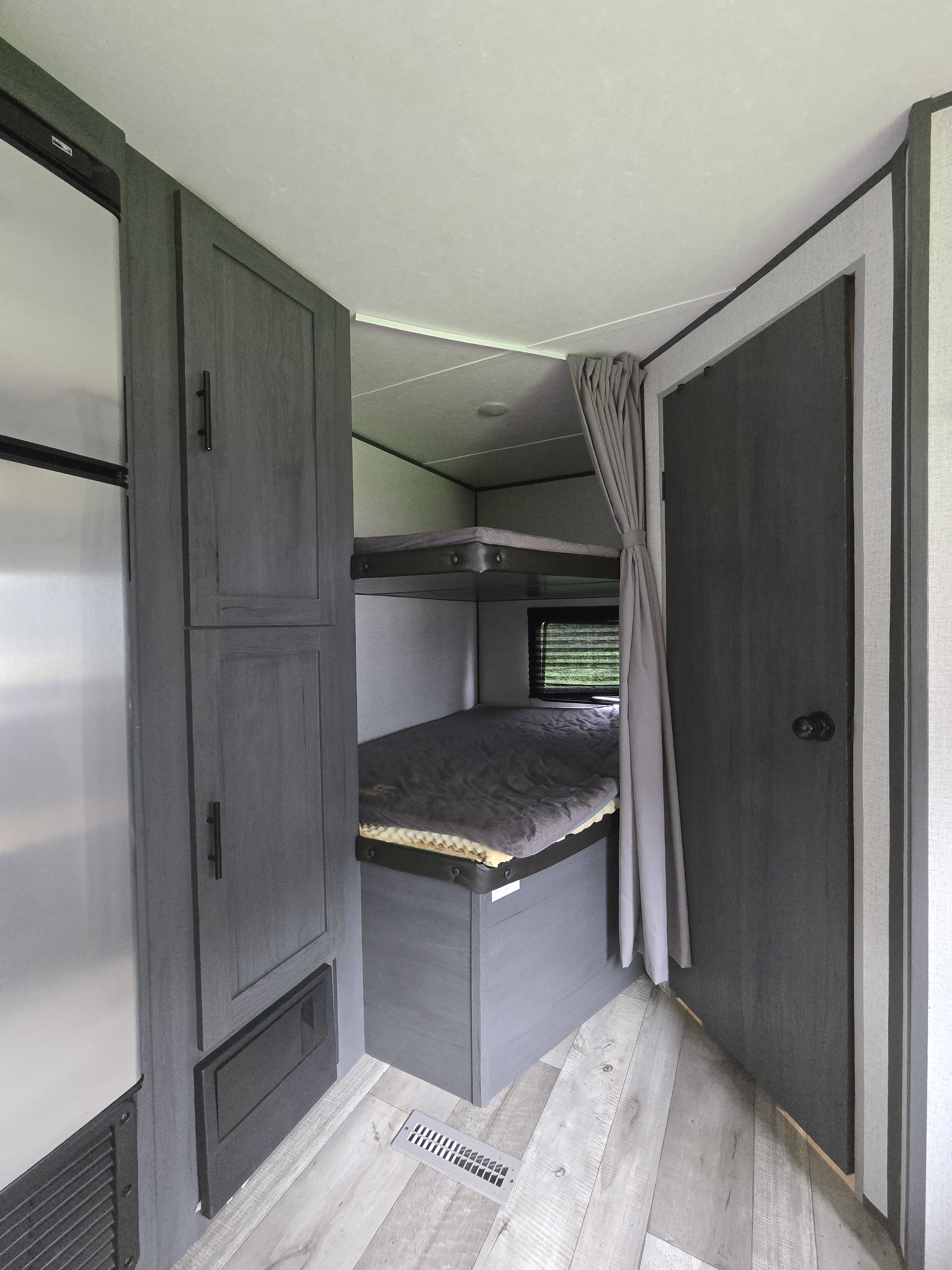 RV rental interior featuring bunk beds with a privacy curtain, adjacent storage, and modern wood-look flooring.. Aspen Trail LE 2021