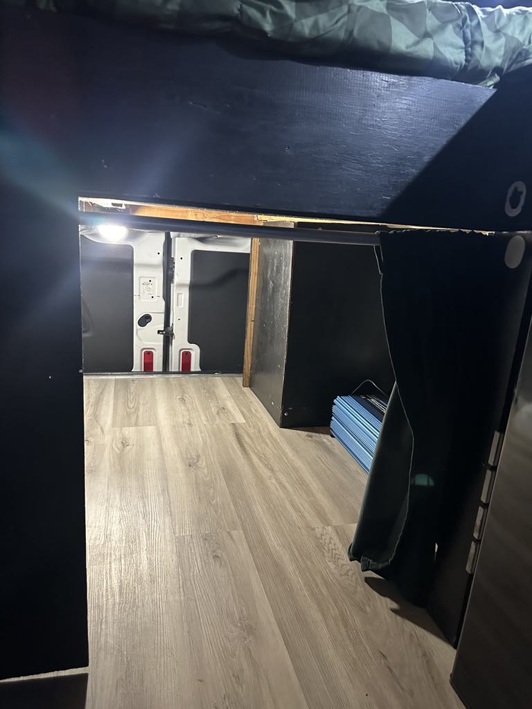 Inside this RV rental: View towards the rear doors, showing the elevated bed platform and light wood-look flooring.. Ford Transit 2017
