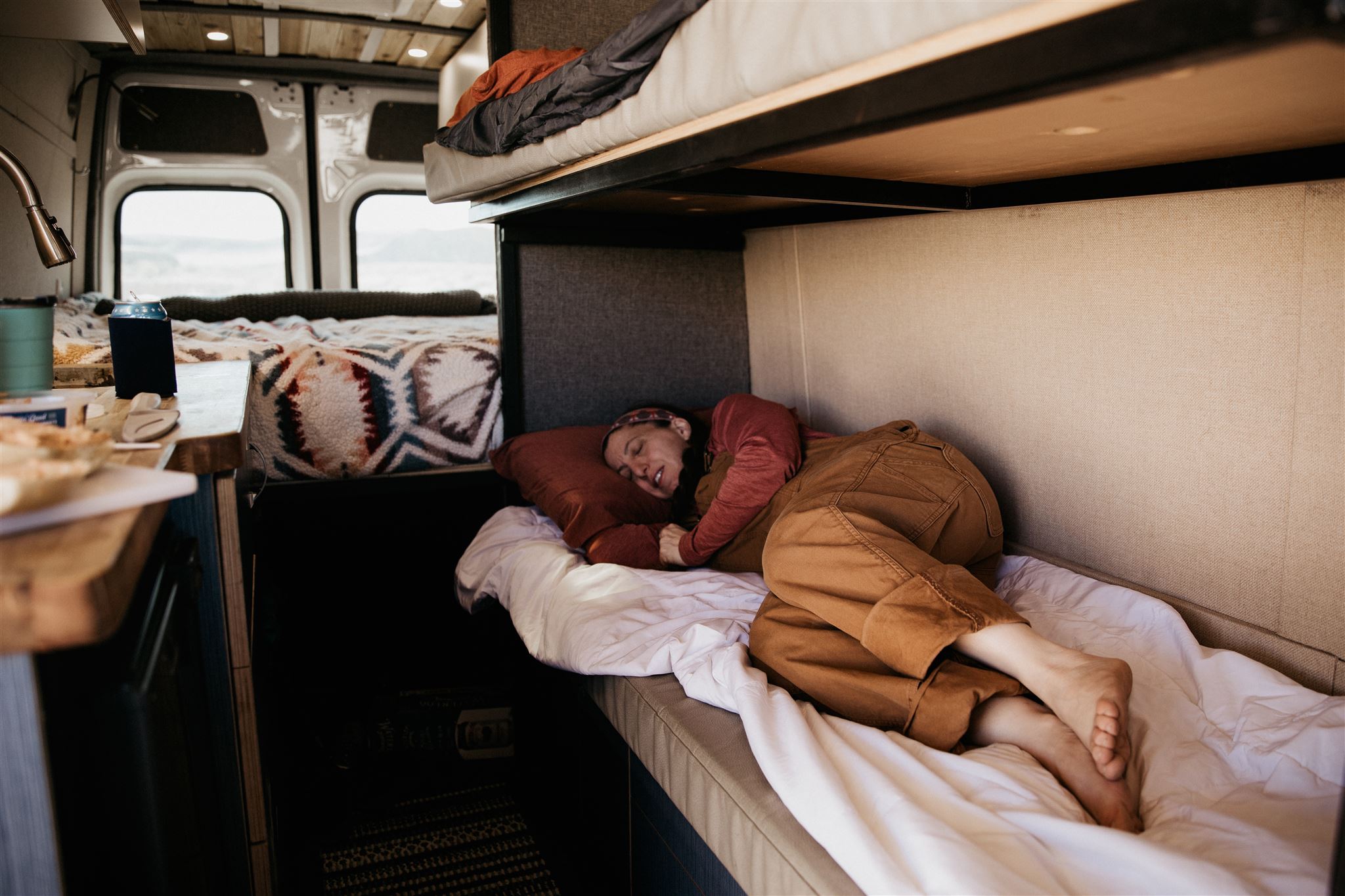 Comfortable RV rental interior: A person sleeps soundly on a lower bunk, with another bed and kitchen area visible, offering cozy van life travel.. Mercedes Mercedes Benz Sprinter Custom Van Conversion 2020