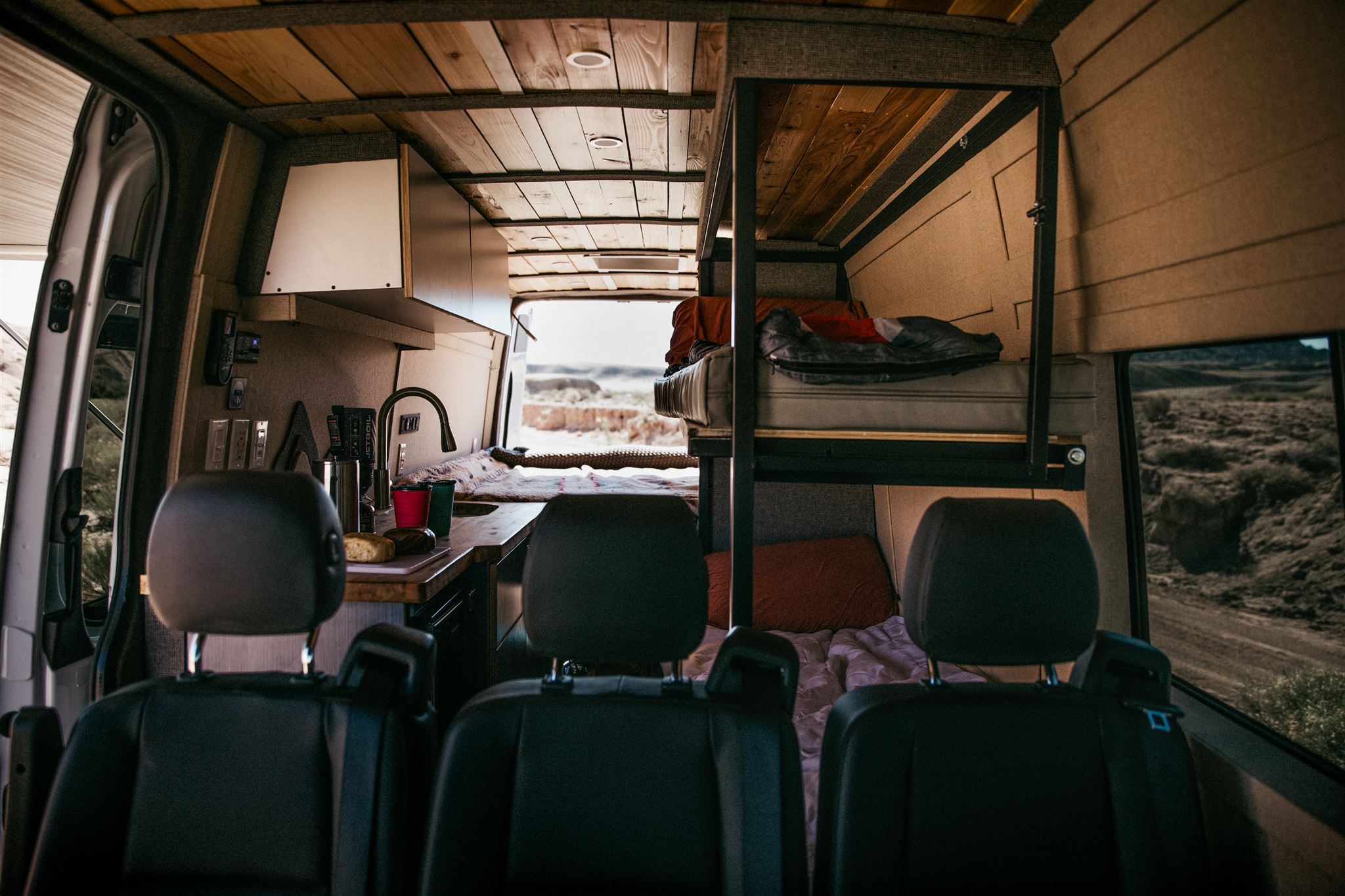 View inside a spacious rv rental van with a full kitchenette, wooden ceiling, and comfortable bunk beds for mobile living.. Mercedes Mercedes Benz Sprinter Custom Van Conversion 2020