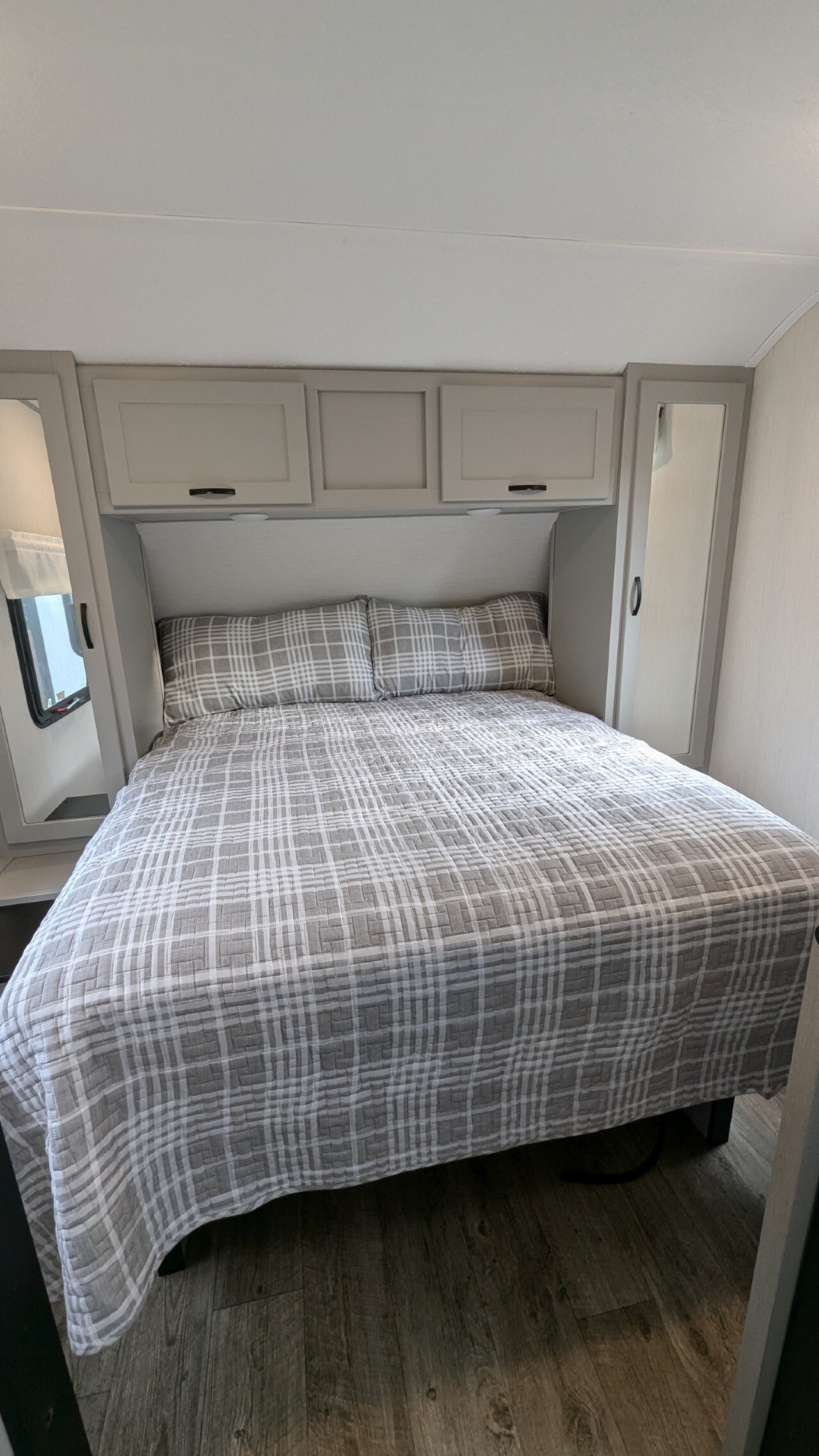 Cozy RV rental bedroom features a bed with gray plaid bedding, overhead cabinets, and side mirrors, perfect for travel.. Forest River Vibe 2022