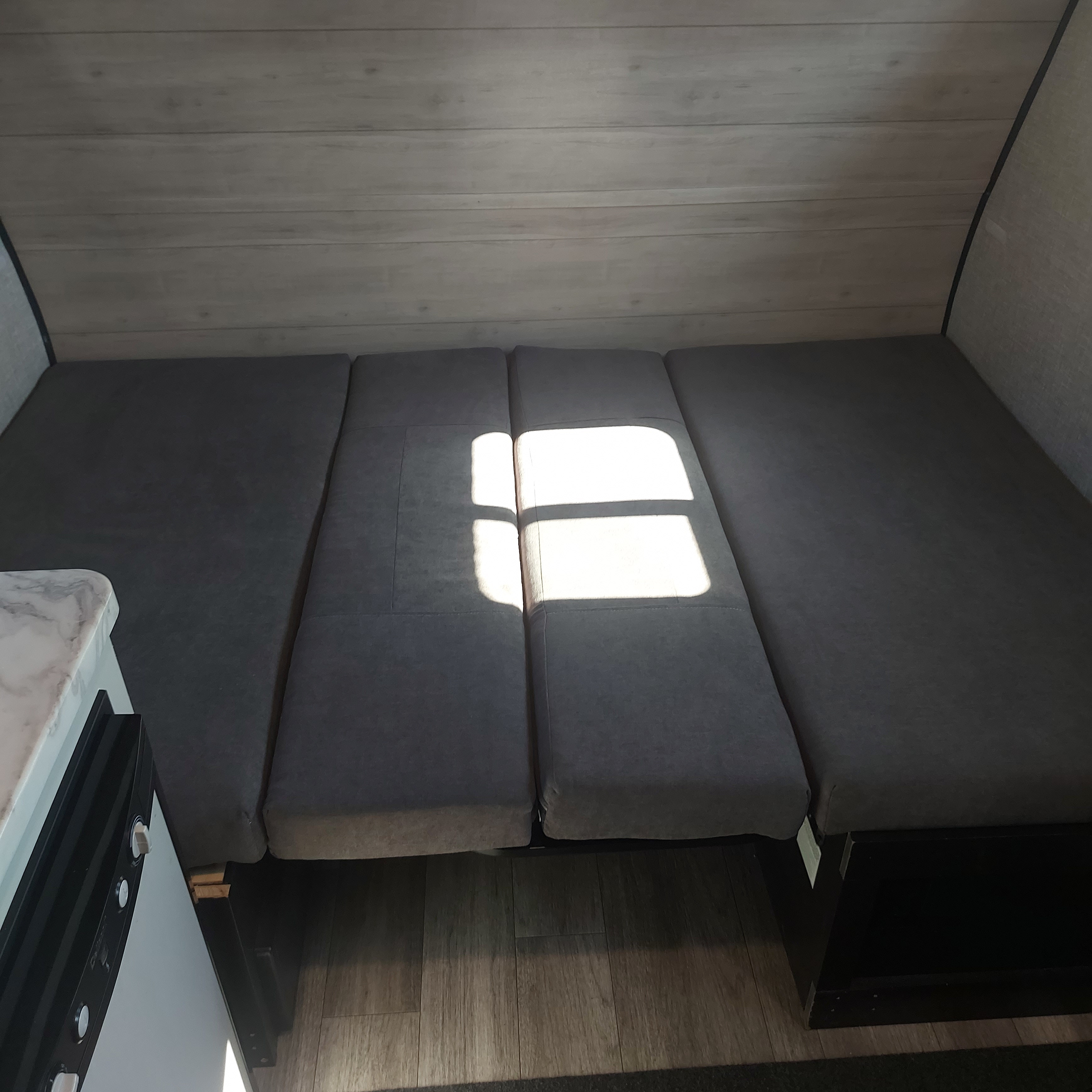 Spacious RV rental interior featuring gray cushions arranged as a bed or seating area, bathed in sunlight, with wood-paneled walls.. Jayco Jay Flight SLX STX Edition 2023