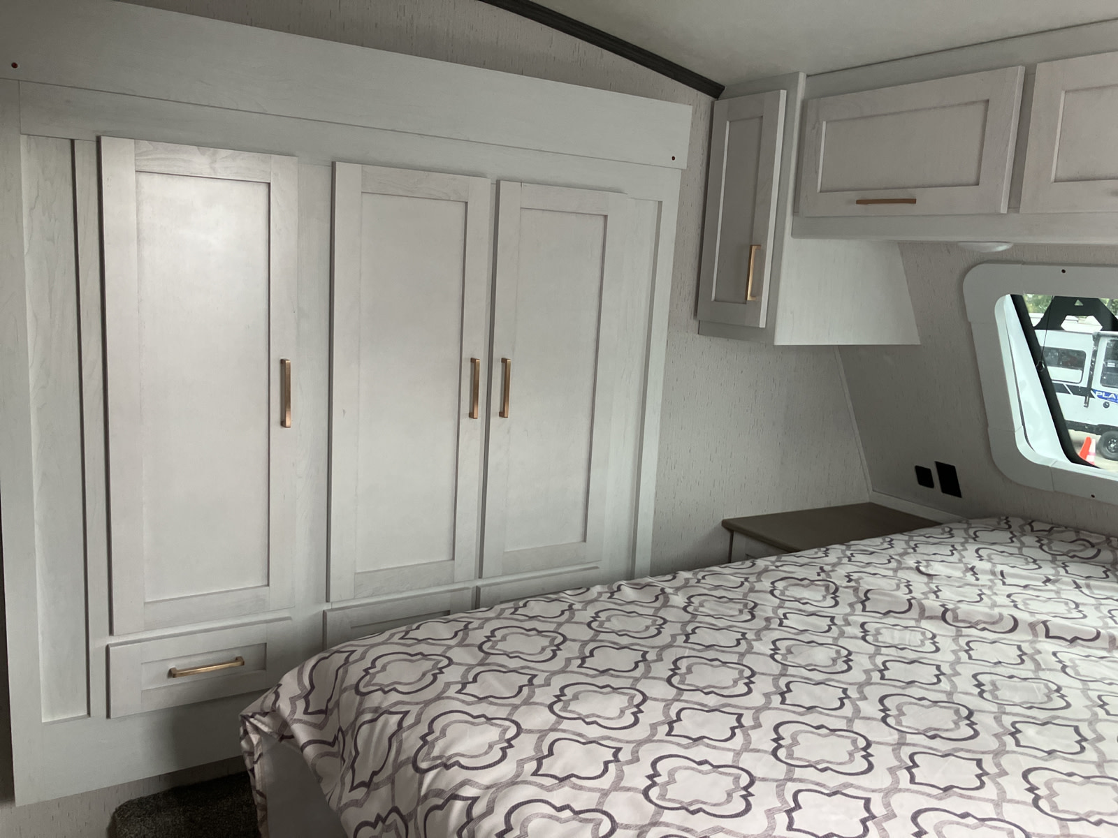 RV rental bedroom with light grey wardrobe, drawers, and overhead cabinets for ample storage. Features a patterned bedspread.. Dutchmen Astoria 2022