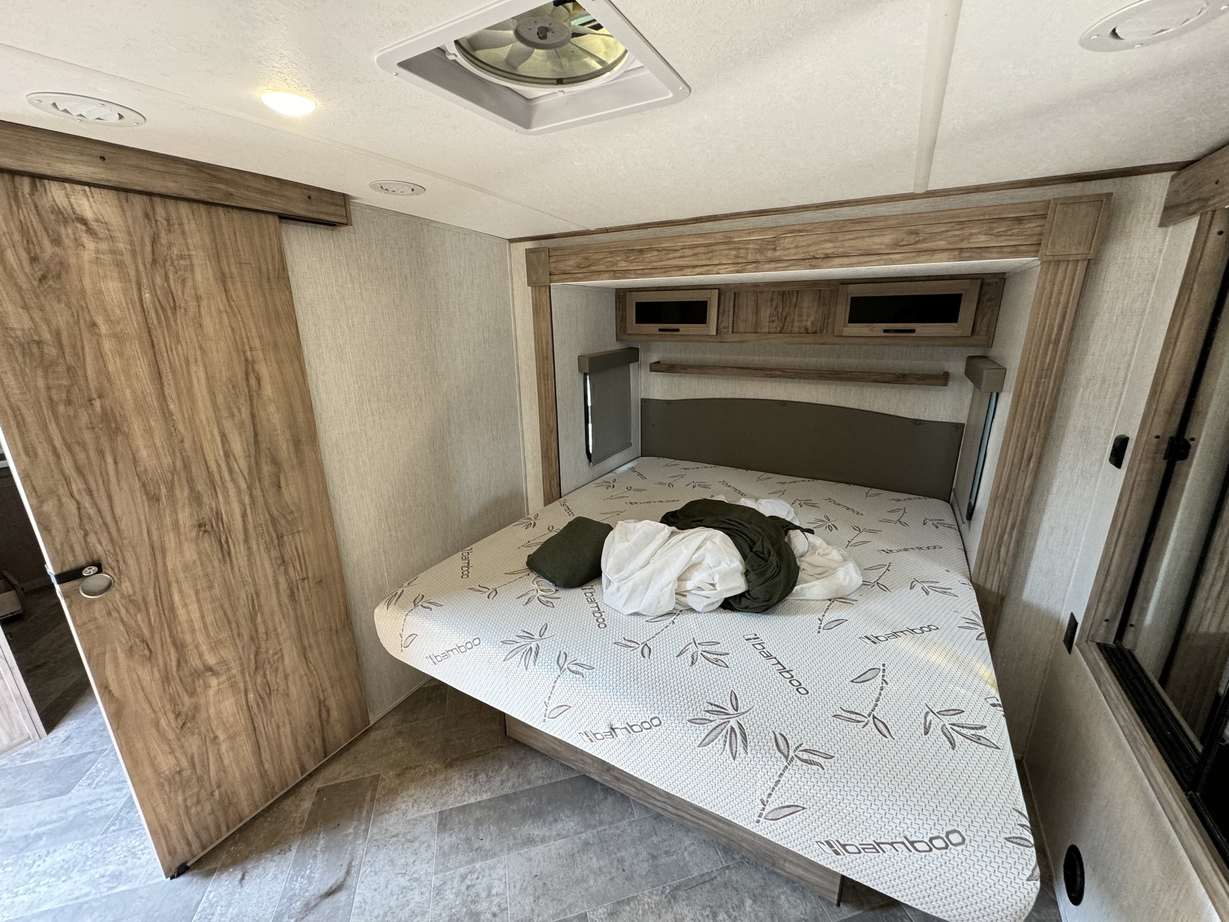 RV rental bedroom with a bamboo-patterned mattress, wood-grain cabinetry, and a sliding door.. Forest River Palomino Solaire 2023