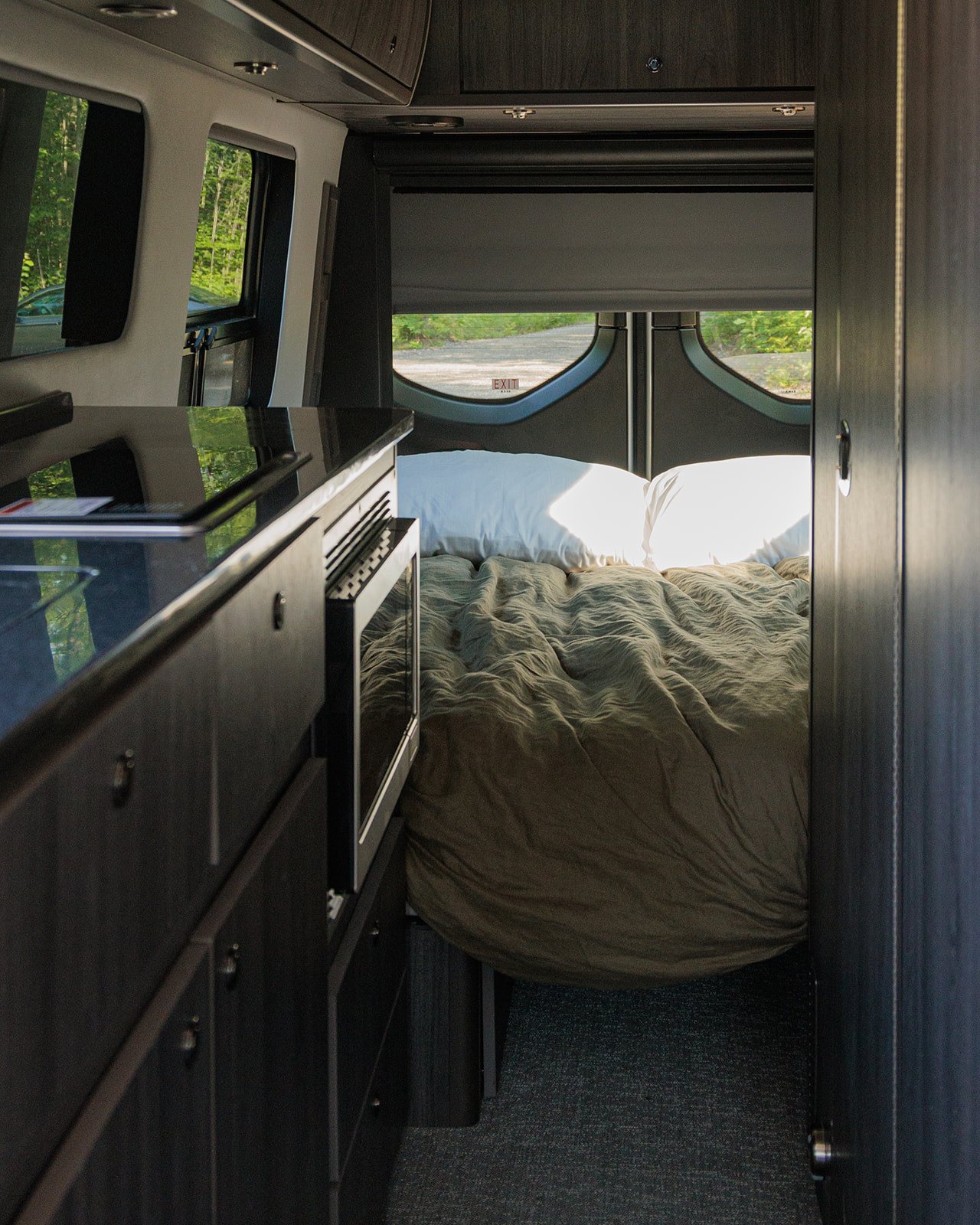 Cozy rv rental interior featuring a comfortable bed, compact kitchen, and scenic outdoor view from the windows.. Grech RV Strada 2023