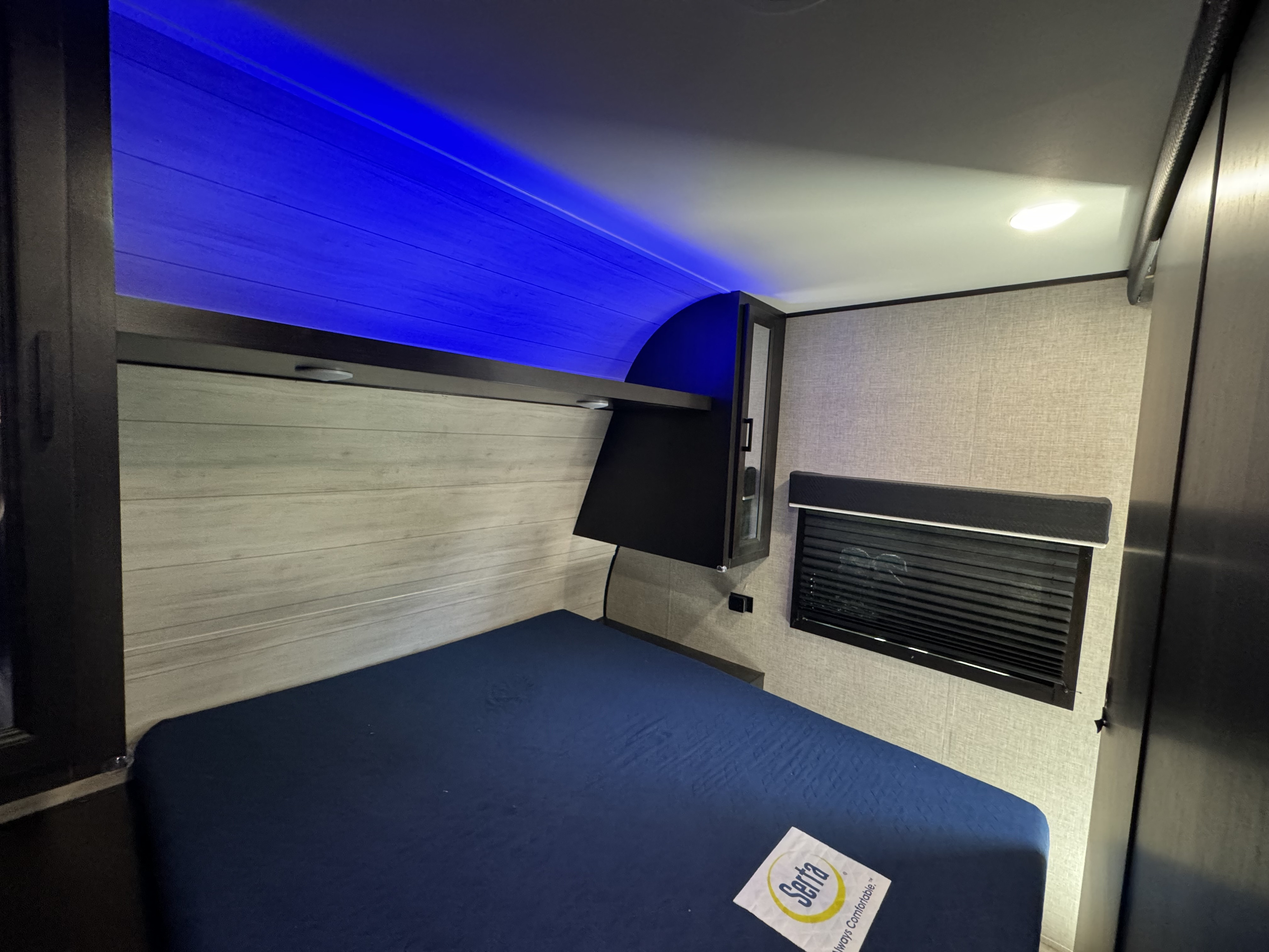 Comfortable RV rental bedroom with dark blue bed, stylish wooden walls, ambient blue lights, and window.. Jayco Jay Flight SLX 2022
