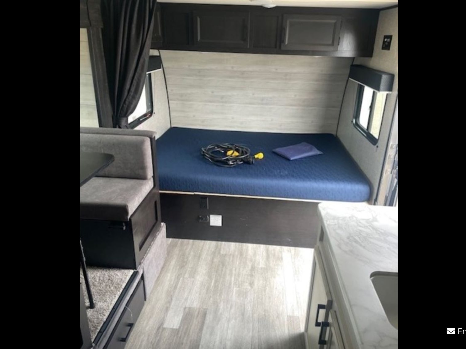 RV rental interior showcasing a bed with blue mattress, gray dinette seating, and kitchenette with sink.. Jayco Jay Flight SLX Baja Edition 2022