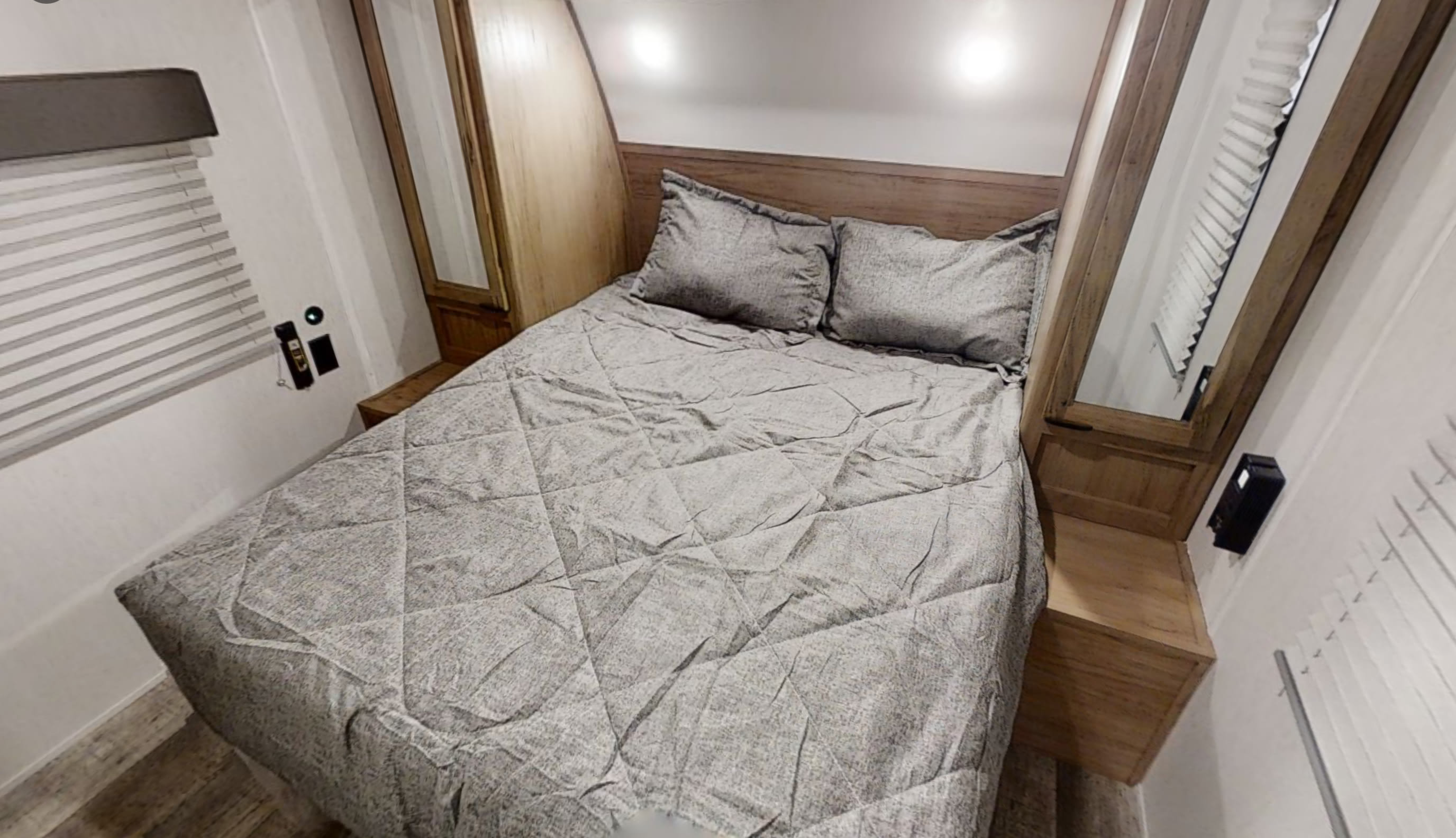 An inviting RV rental bedroom. It features a quilted gray bed, wooden headboard, and mirrored side cabinets with lighting.. Forest River Cherokee Grey Wolf 2022