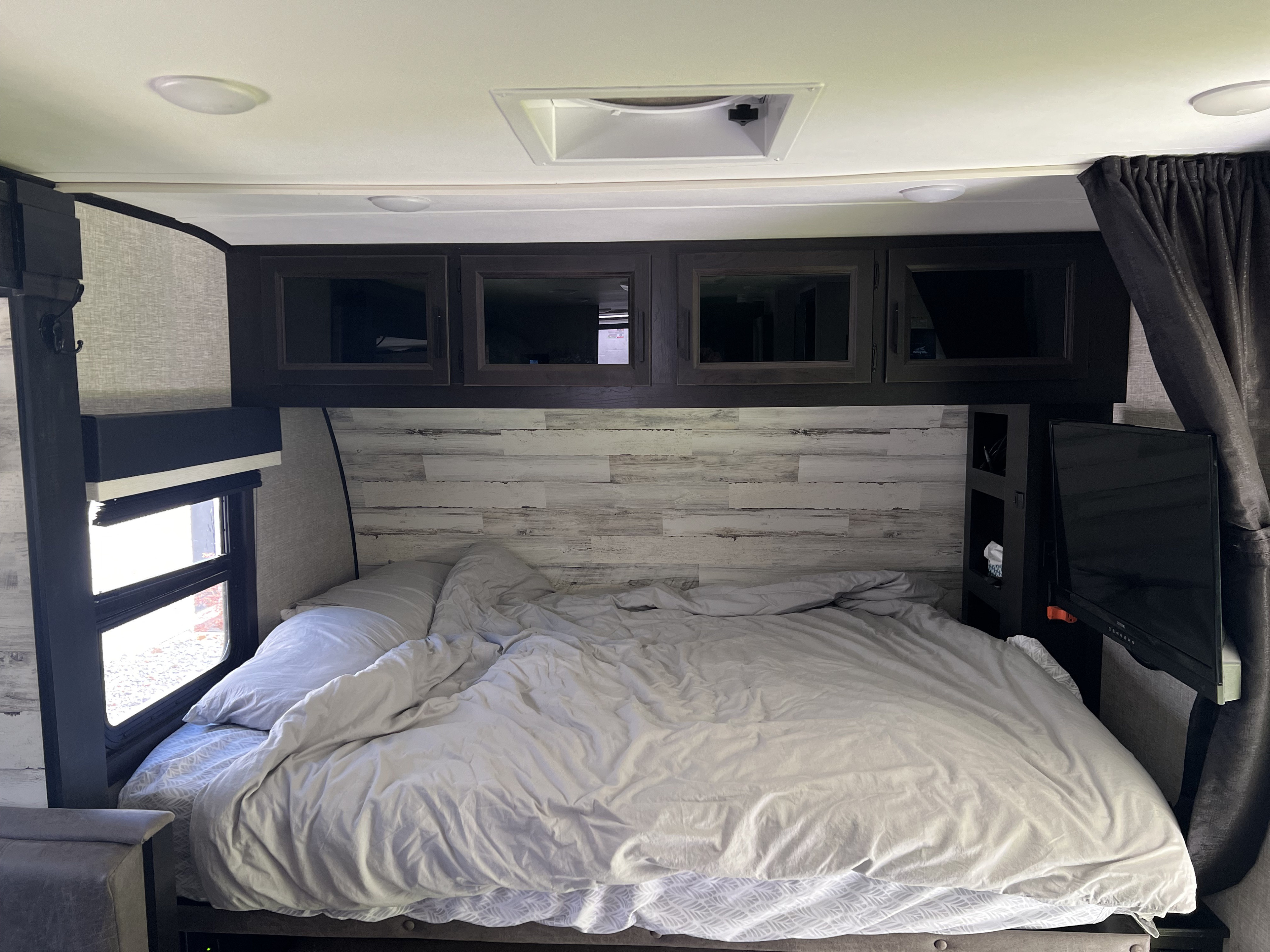 Cozy RV rental bedroom interior with a comfortable bed, overhead cabinets, window blinds, and a mounted TV.. Jayco Jay Feather Micro 2022