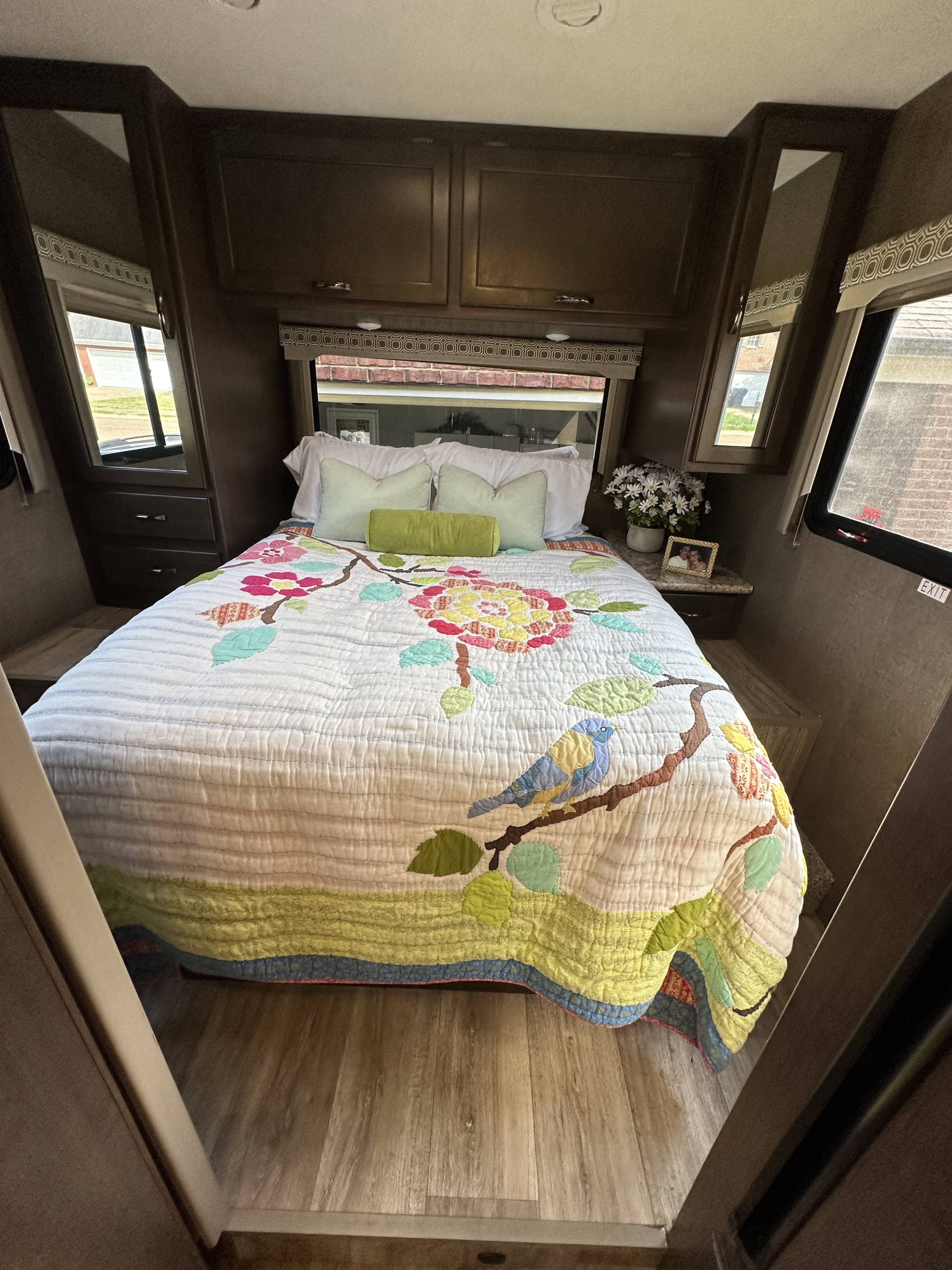 Cozy RV rental bedroom, featuring a colorful quilt, white & green pillows, ample storage, and natural light.. Thor Four Winds 2020
