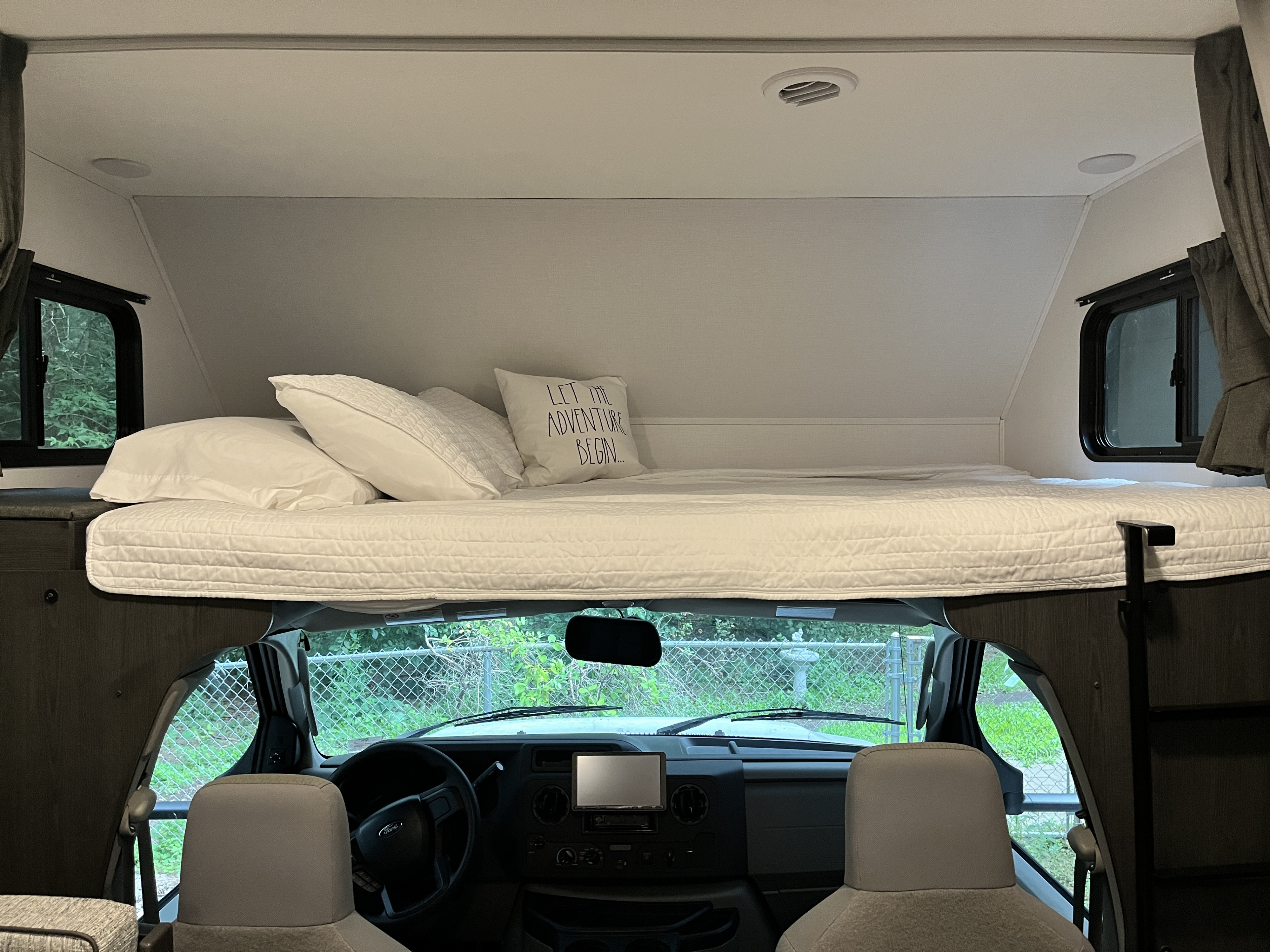 This rv rental features a cozy cabover bunk bed with white bedding, above the driver's cockpit. Ideal for your next adventure.. Forest River Solera 27 DSE 2023