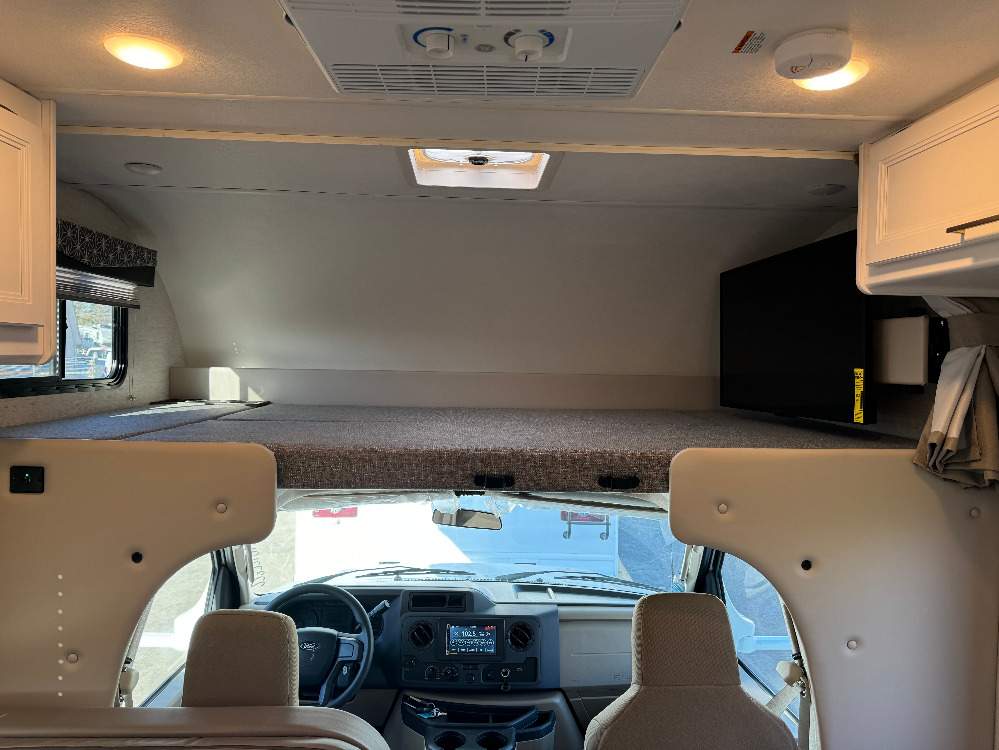 Spacious RV rental interior featuring an overhead bunk bed, wall-mounted TV, and a clear view of the driver's cockpit.. Thor Freedom Elite 2024