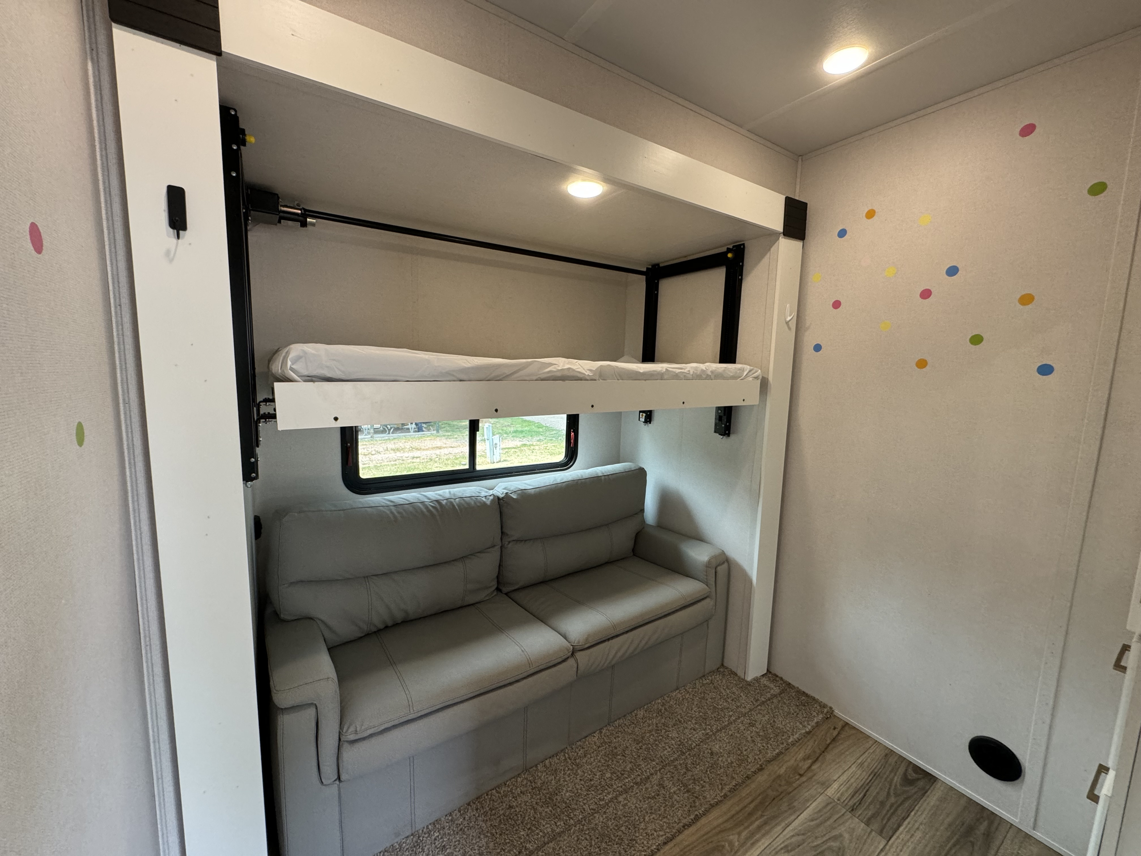 RV rental interior featuring a versatile bunk bed over a cozy gray sofa, with a window and playful polka dot wall decals.. Prime Time Crusader 2021