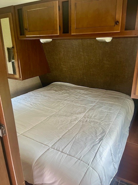 This RV rental bedroom features a large bed with a white comforter, wooden overhead cabinets, and built-in reading lights.. Heartland RVs Prowler 2014