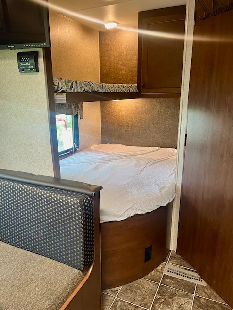 Cozy bunk beds and living space inside an RV rental, featuring a lower bed, upper bunk, and nearby sofa.. Heartland RVs Prowler 2014