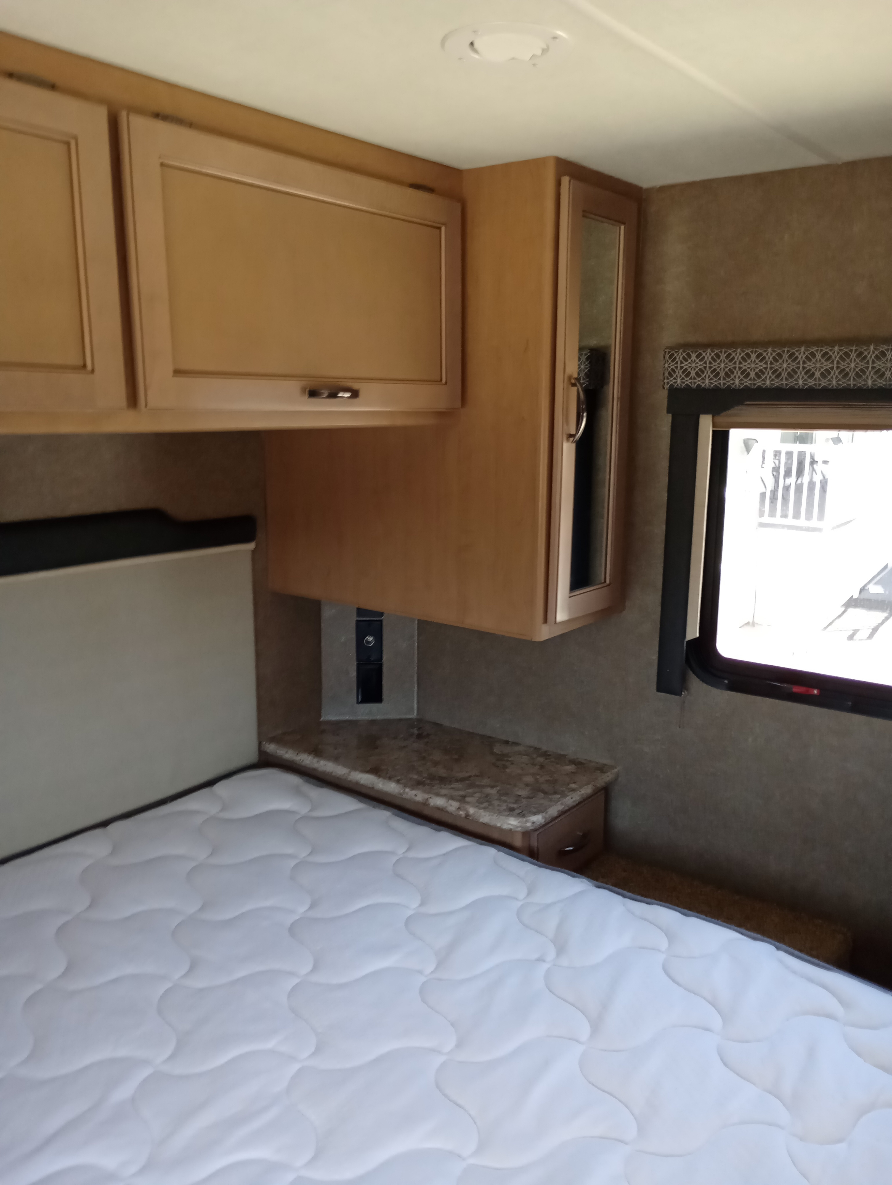 Cozy RV rental bedroom featuring a comfy bed, overhead cabinets, a nightstand with outlets, and a window for natural light.. Thor Motor Coach Four Winds 2021
