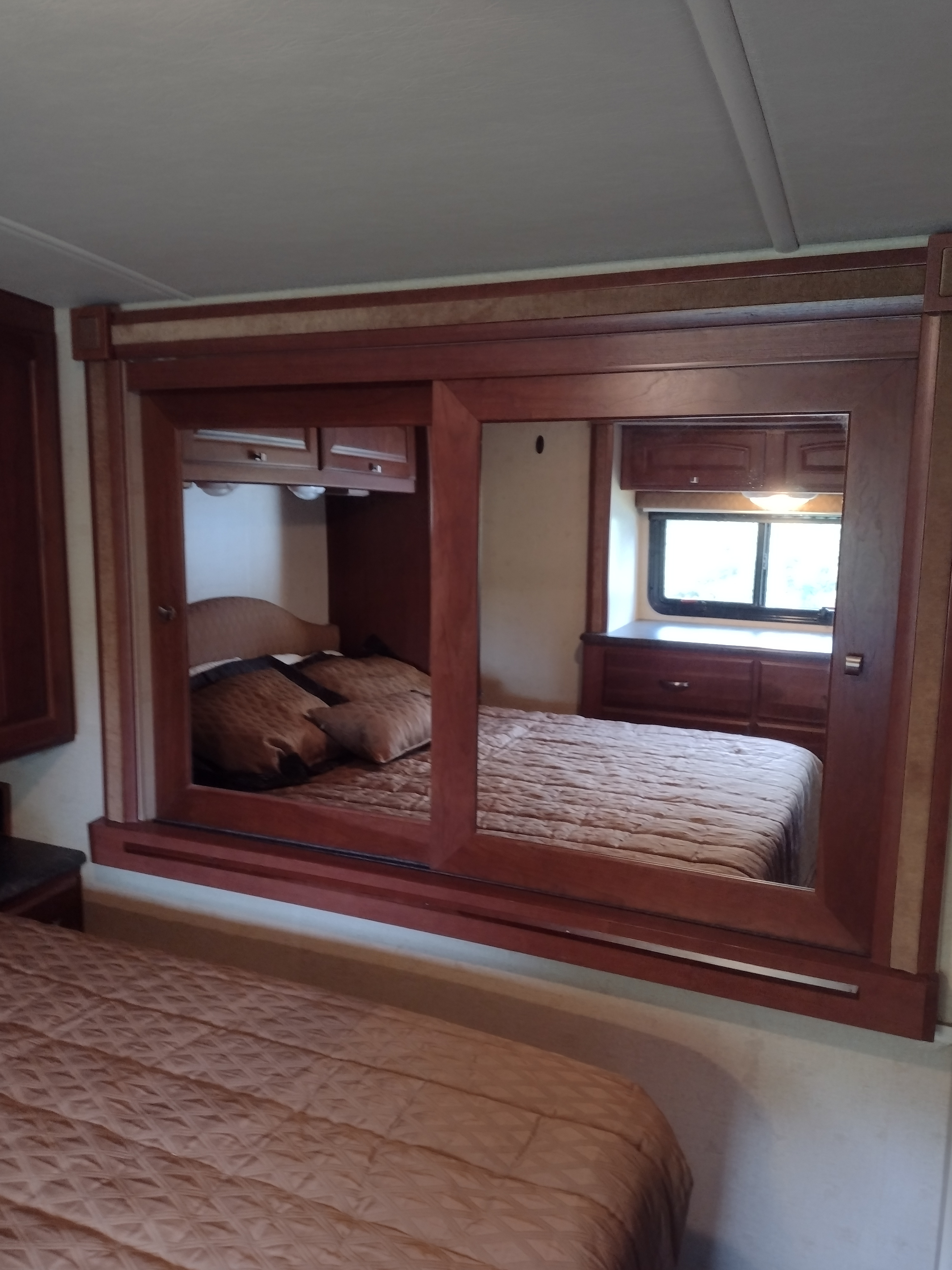 RV rental bedroom interior featuring a large mirror, cozy bed, window with natural light, and built-in storage.. Winnebago Vista 2013