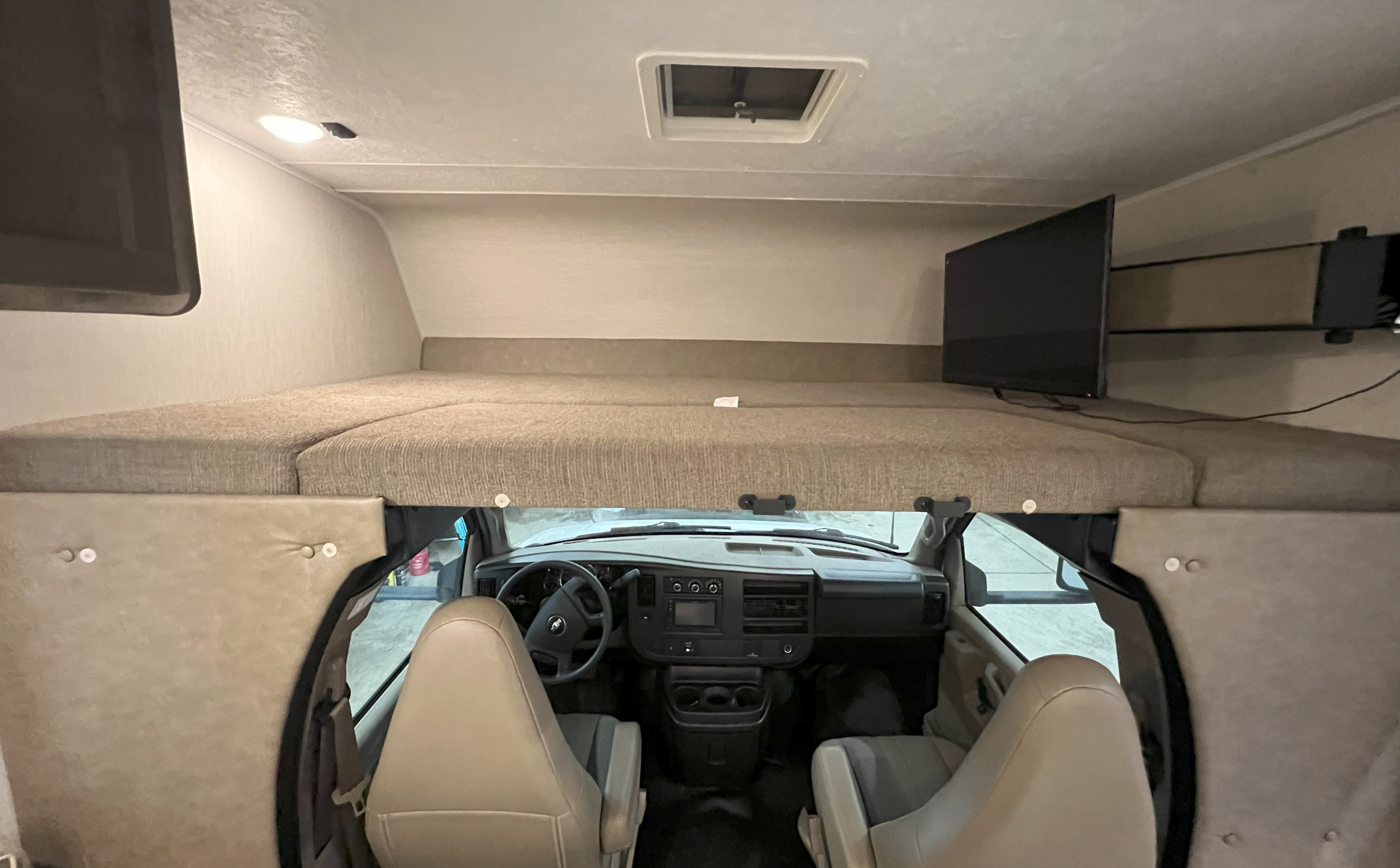 Inside an RV rental: view of the comfy cab-over bunk bed, front cockpit, ceiling vent, and TV.. Coachmen Freelander 2020