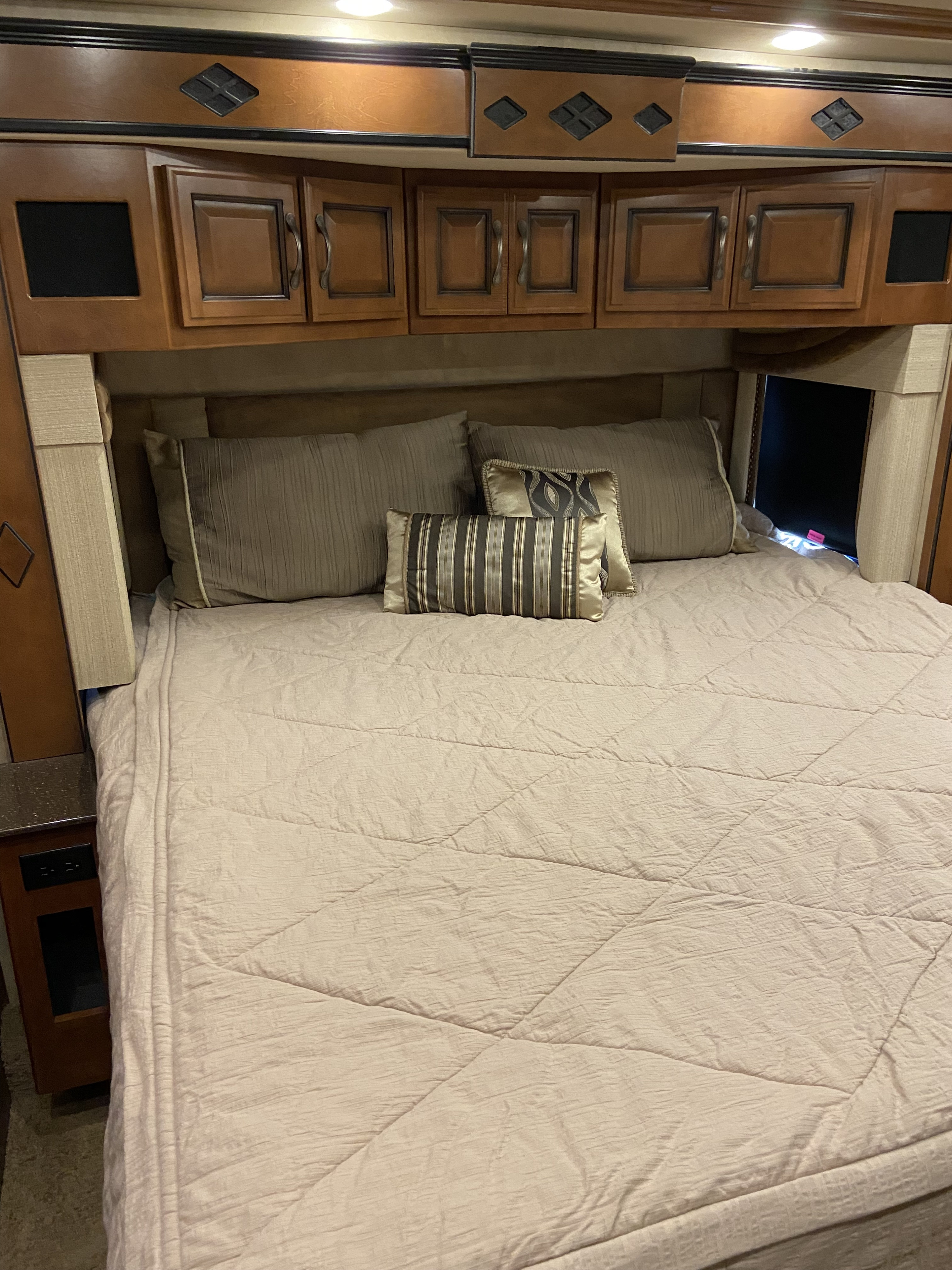 RV rental bedroom: a cozy bed with decorative pillows and functional wooden overhead cabinets, complete with accent lighting.. Fleetwood Other 2015