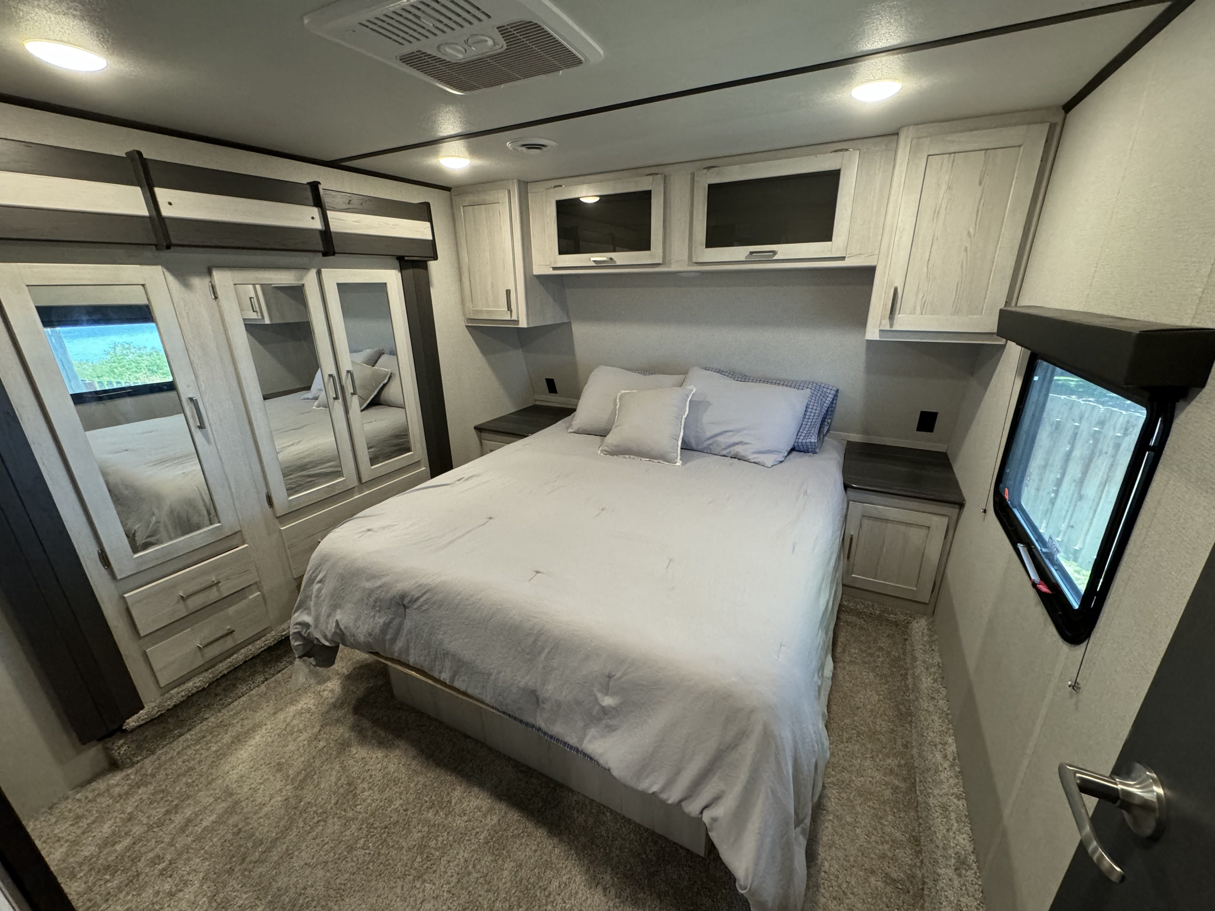 A comfortable RV rental bedroom features a queen bed with light gray bedding, mirrored wardrobe, and overhead cabinets.. Keystone RV Sprinter Limited 2021