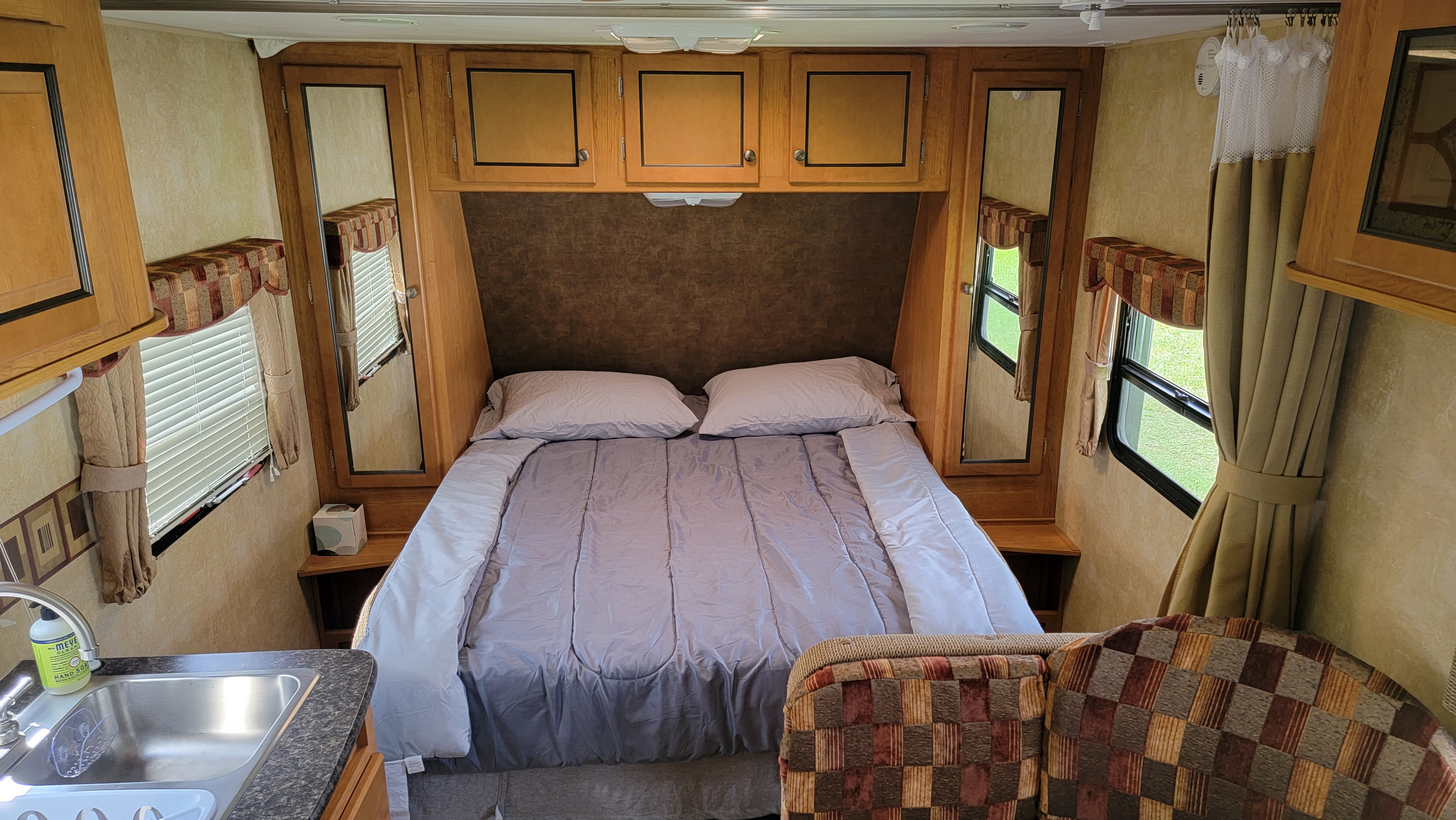 Inside an RV rental: a cozy bedroom setup with a bed, wood cabinets, and large windows. Sink and patterned chair also visible.. Navistar R-Vision Trail-Sport 2013