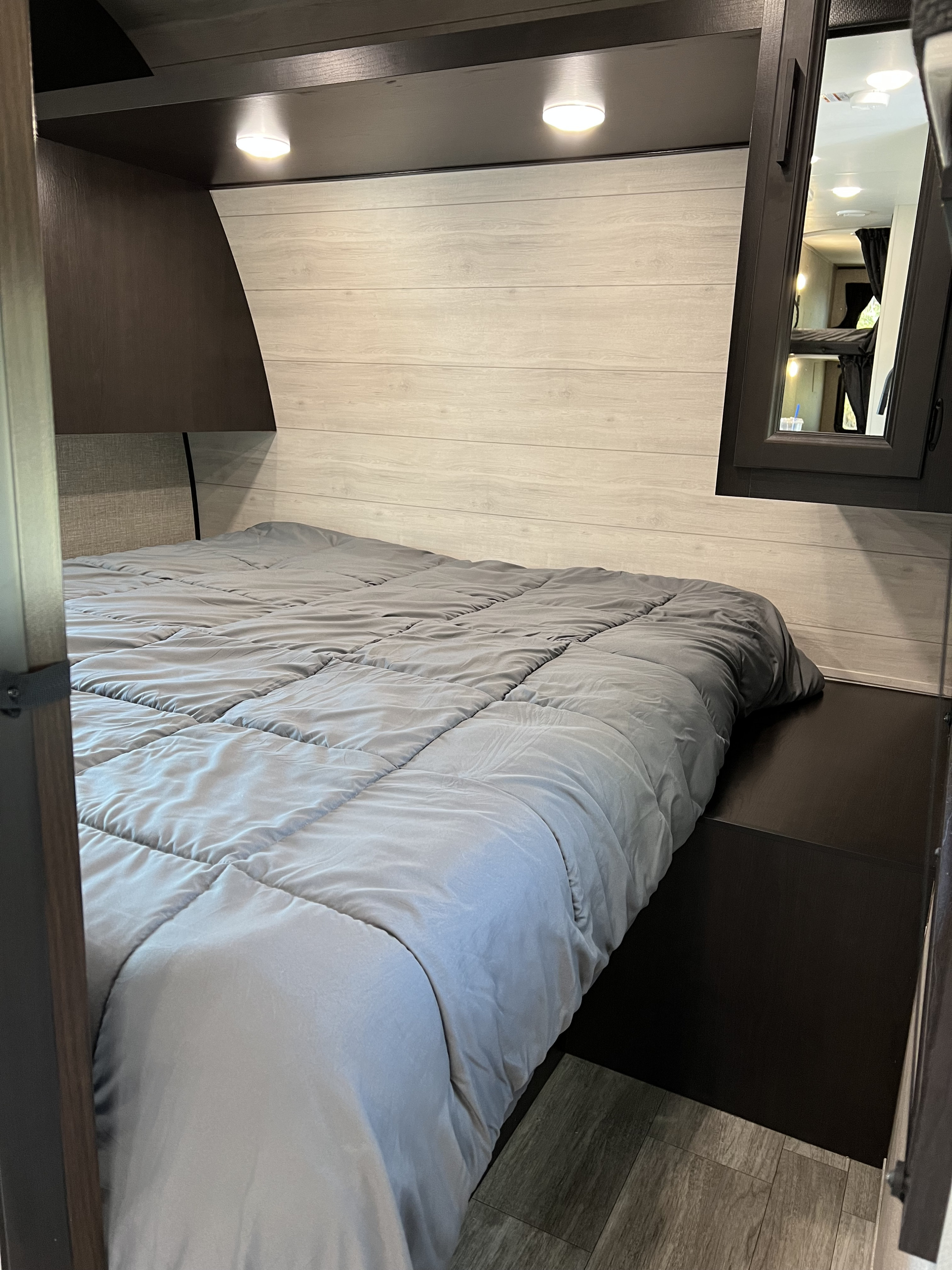 RV rental bedroom showcasing a gray bed, light wood paneling, overhead lights, and dark built-in storage.. Jayco Jay Flight 2023