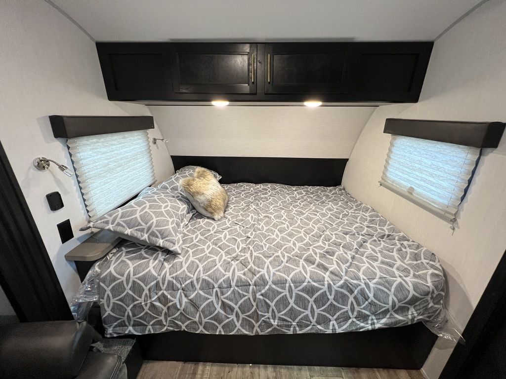 Cozy RV rental bedroom with patterned queen bed, overhead storage, and window blinds for comfort.. Forest River Cherokee Wolf Pup Black Label 2022