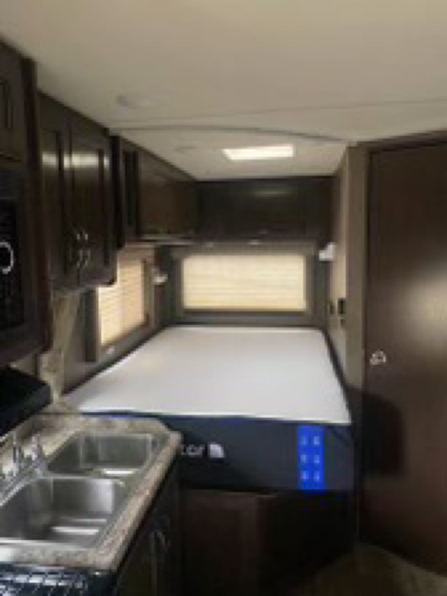 RV rental interior features a kitchen sink, dark wood cabinets, and a comfortable bed with windows.. Thor Motor Coach Four Winds 2018