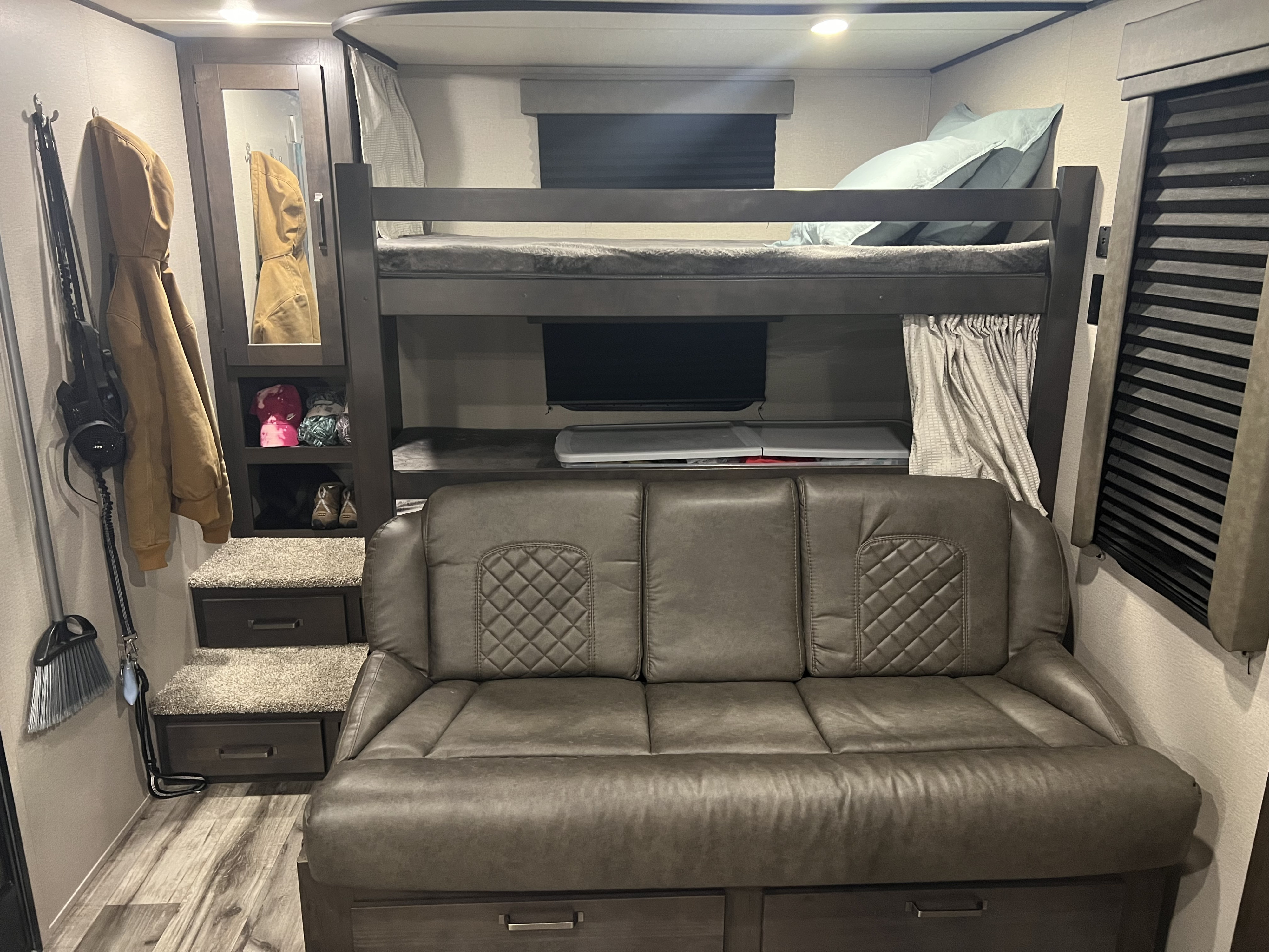 RV rental interior: cozy bunk beds over a couch, storage stairs, and compact living space with a mirror.. Grand Design Transcend Xplor 2022