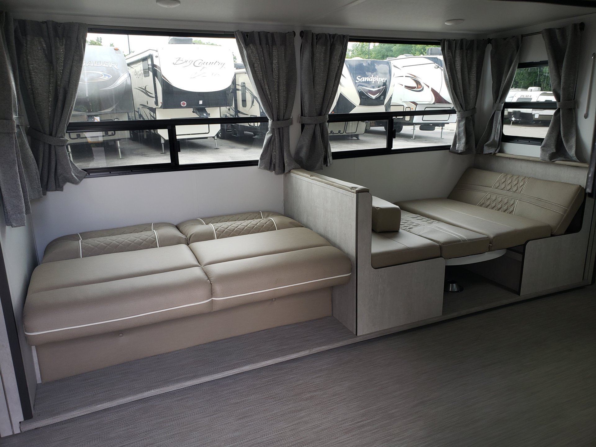 Spacious RV rental interior with light beige dinette and convertible sofa seating. Large windows reveal other RVs outside, ready for travel.. Travel Lite Evoke 2020